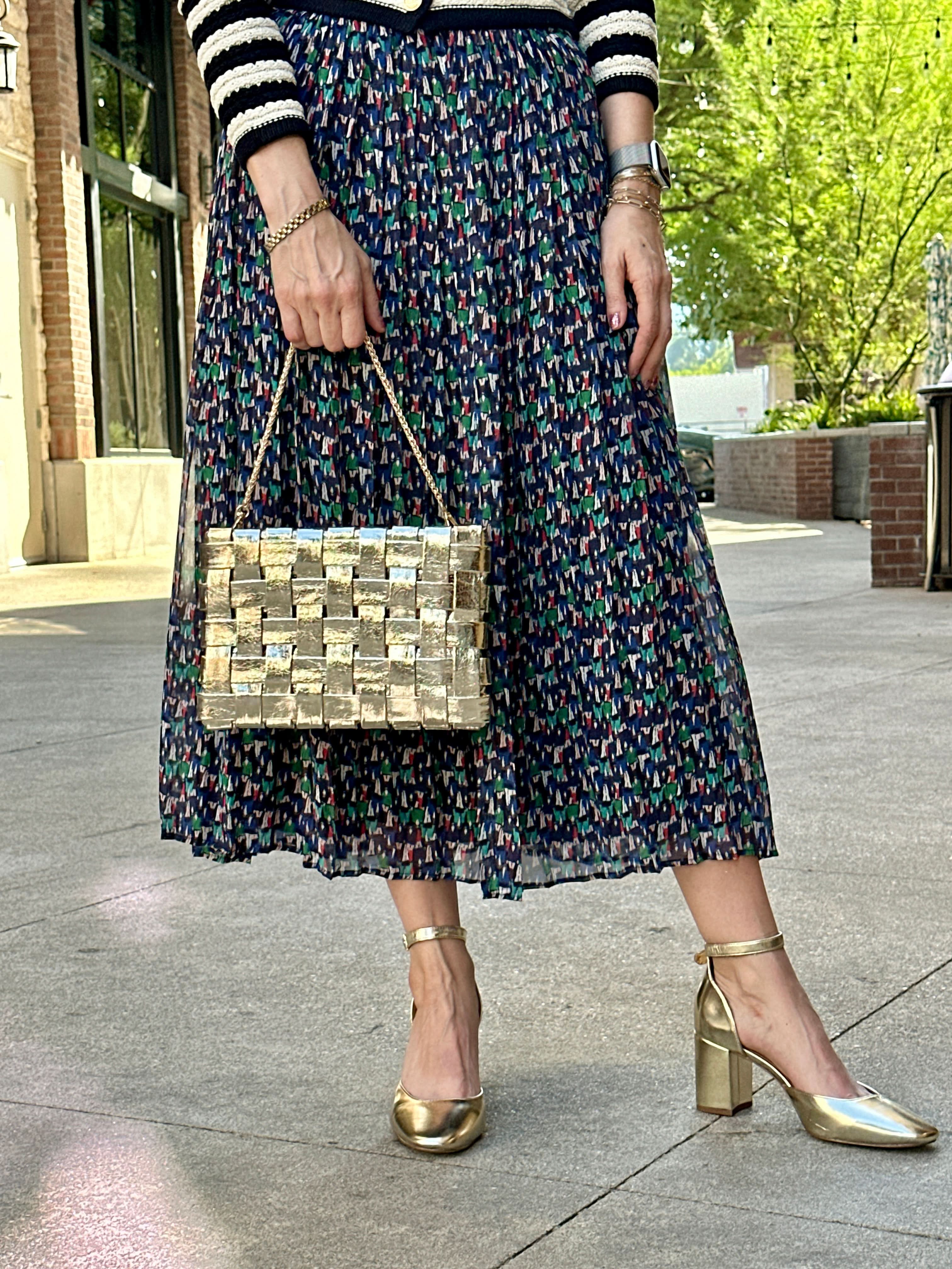 Woman in patterned skirt holding a gold Lindy woven clutch by the strap
