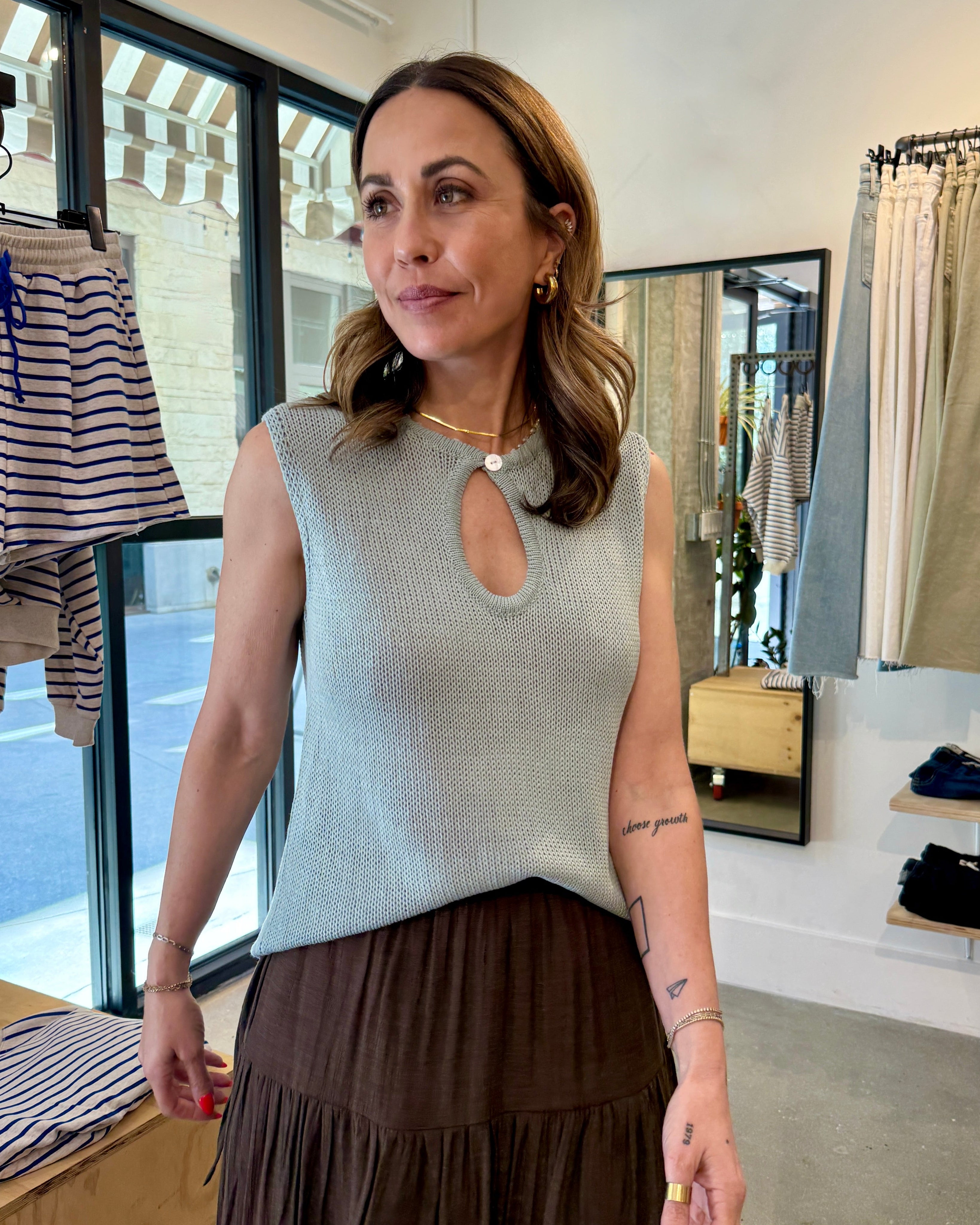 Woman standing in a clothing store wearing a sleeveless top and skirt.