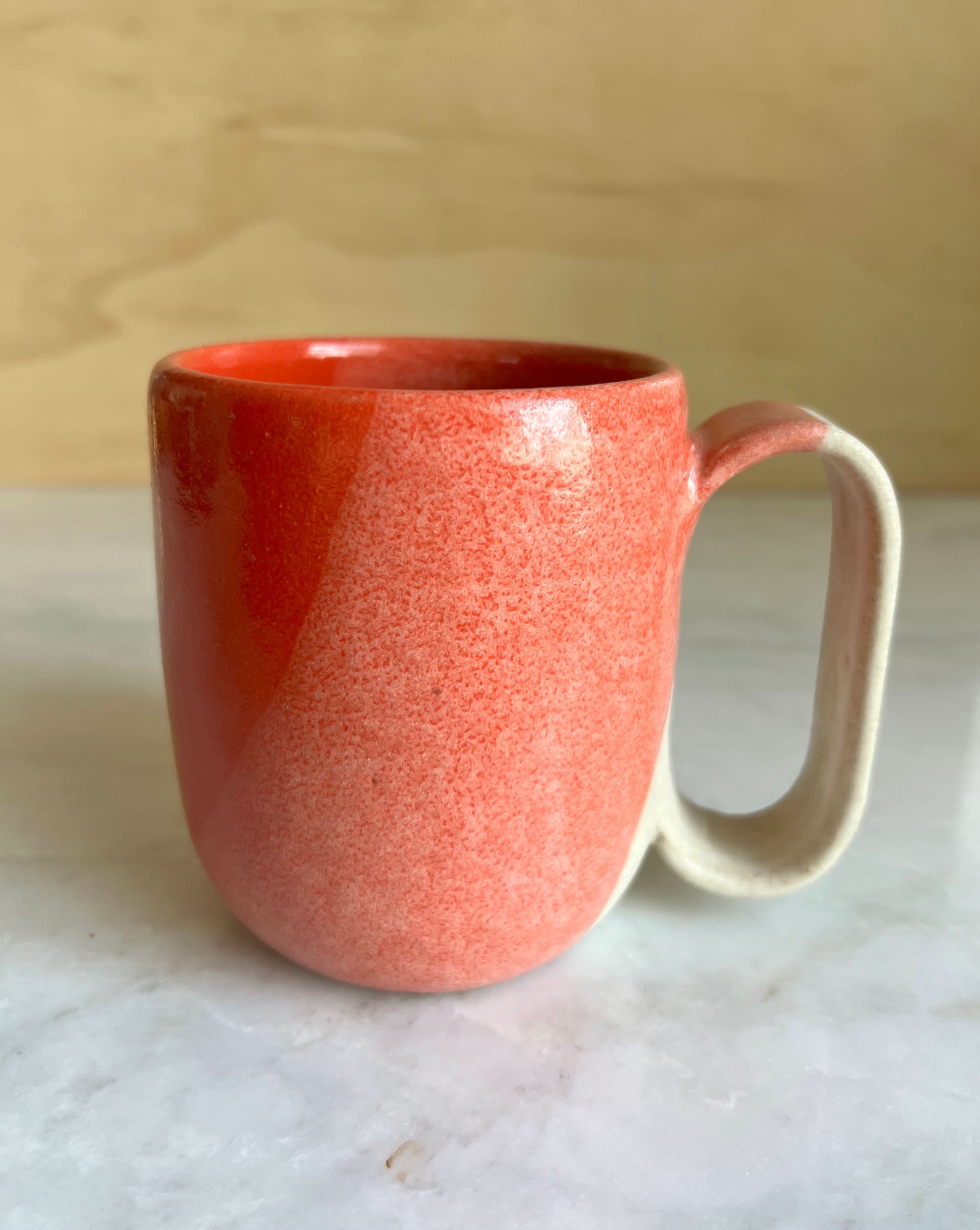 Red ceramic mug with a white handle on a marble surface