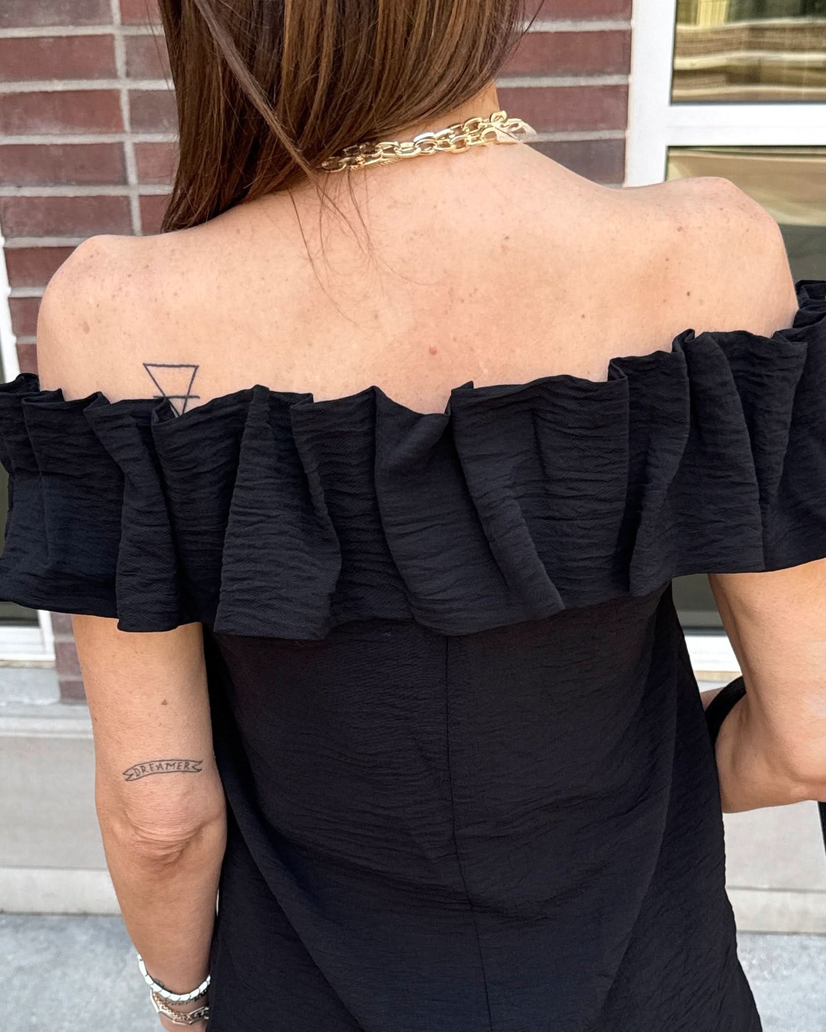 Woman with her back turned wearing a black off the shoulder ruffle top.