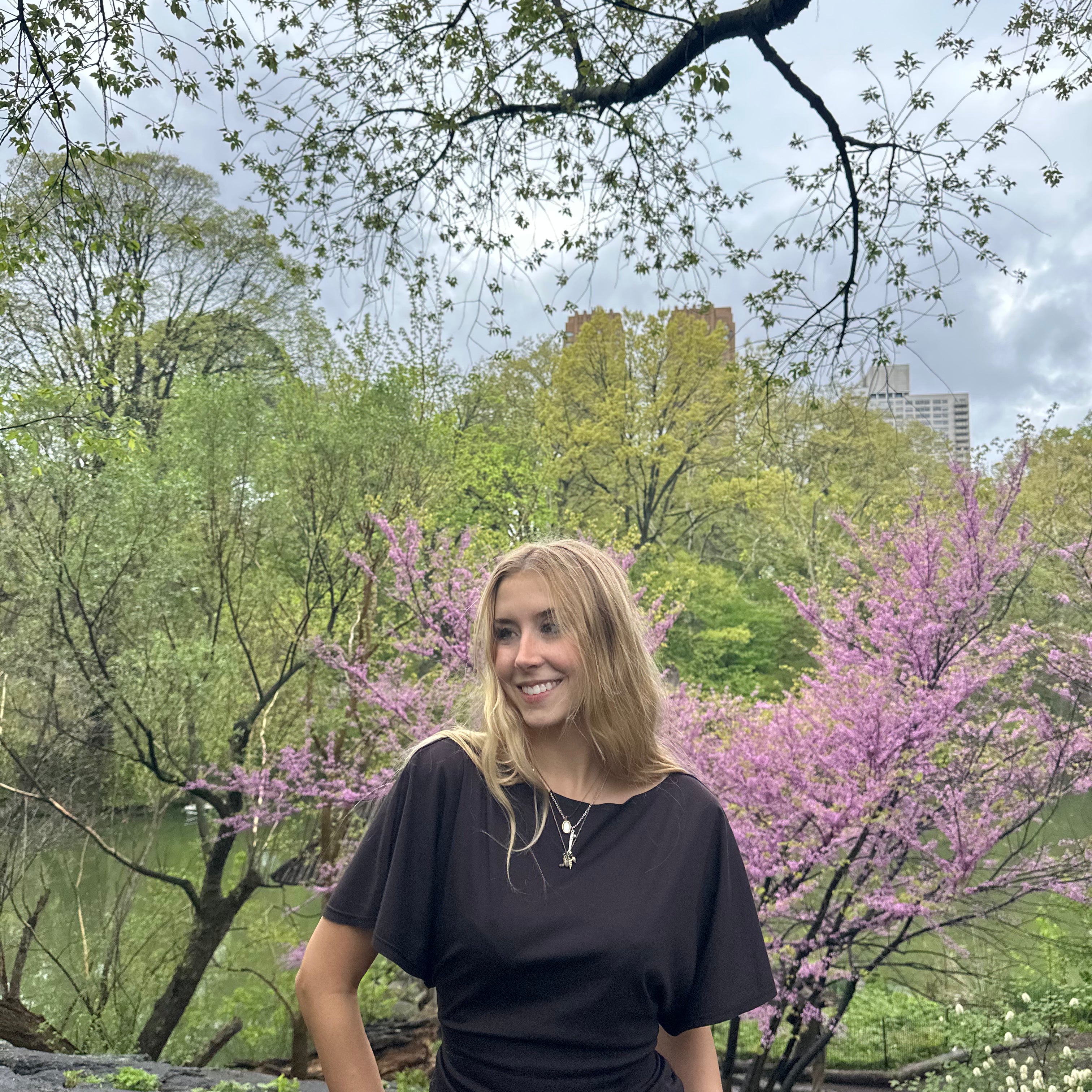 Woman standing in a park with trees and pink flowers in the background