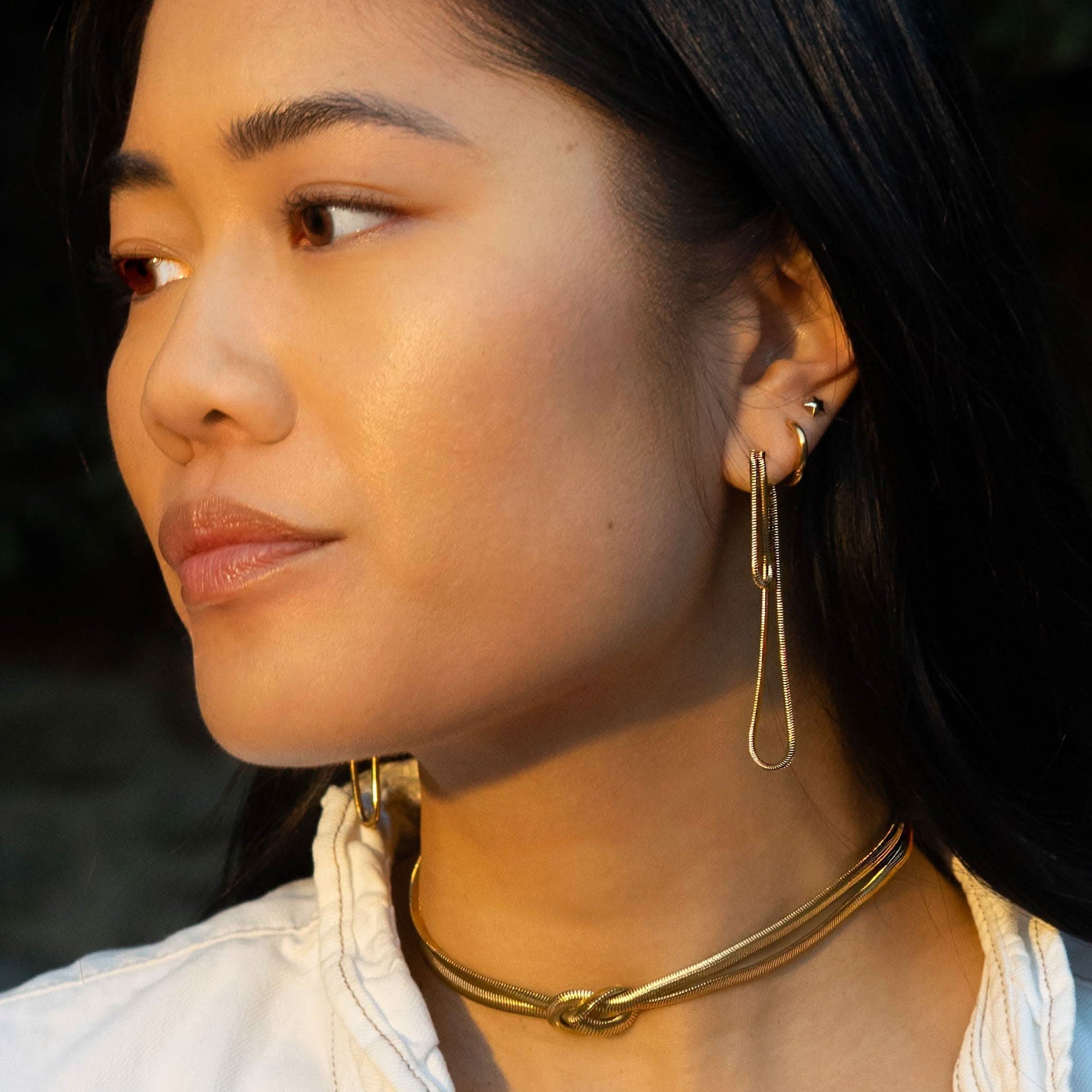 Woman wearing long abstract loop earrings and gold figure.