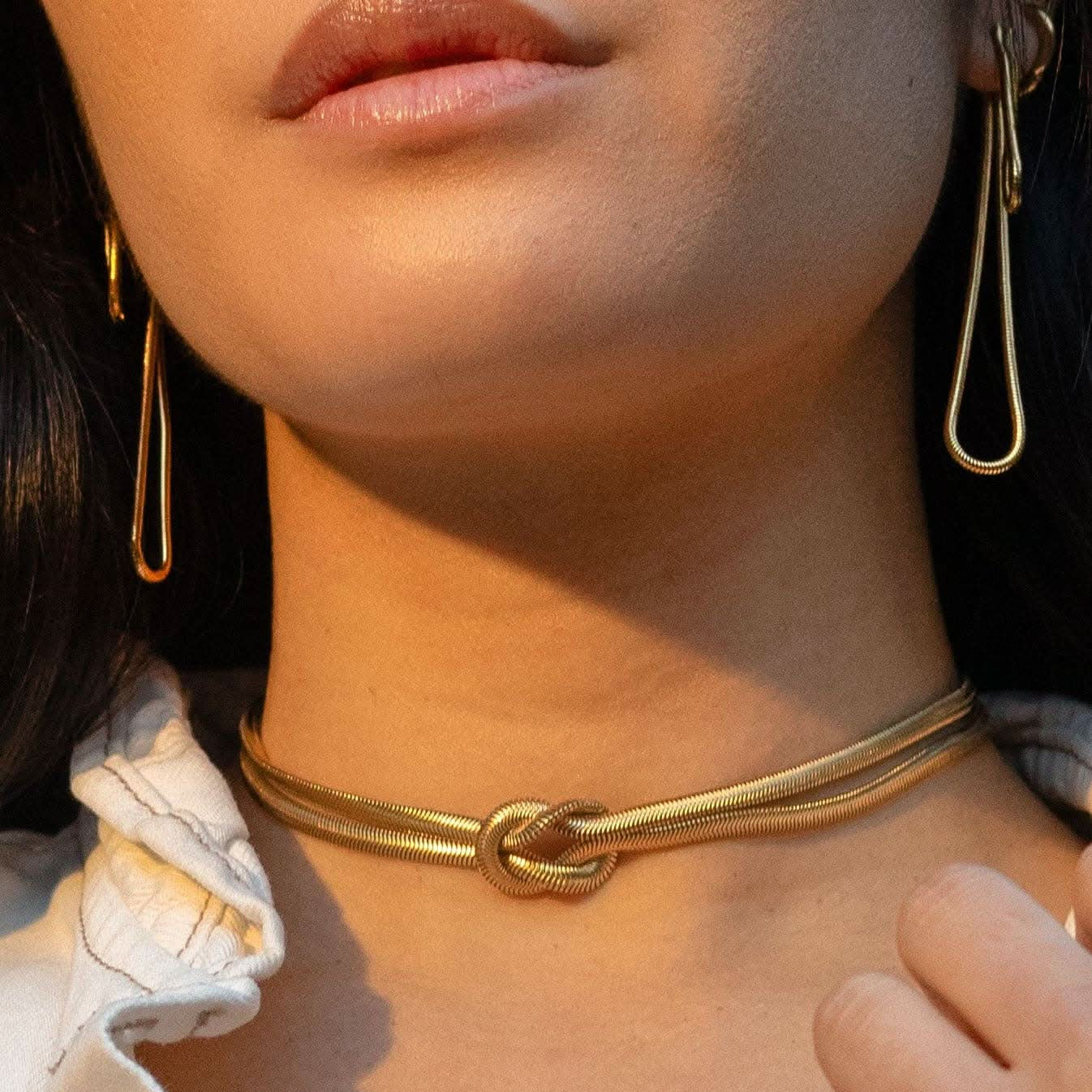 Woman wearing long abstract loop earrings and gold figure eight knot herringbone choker necklace