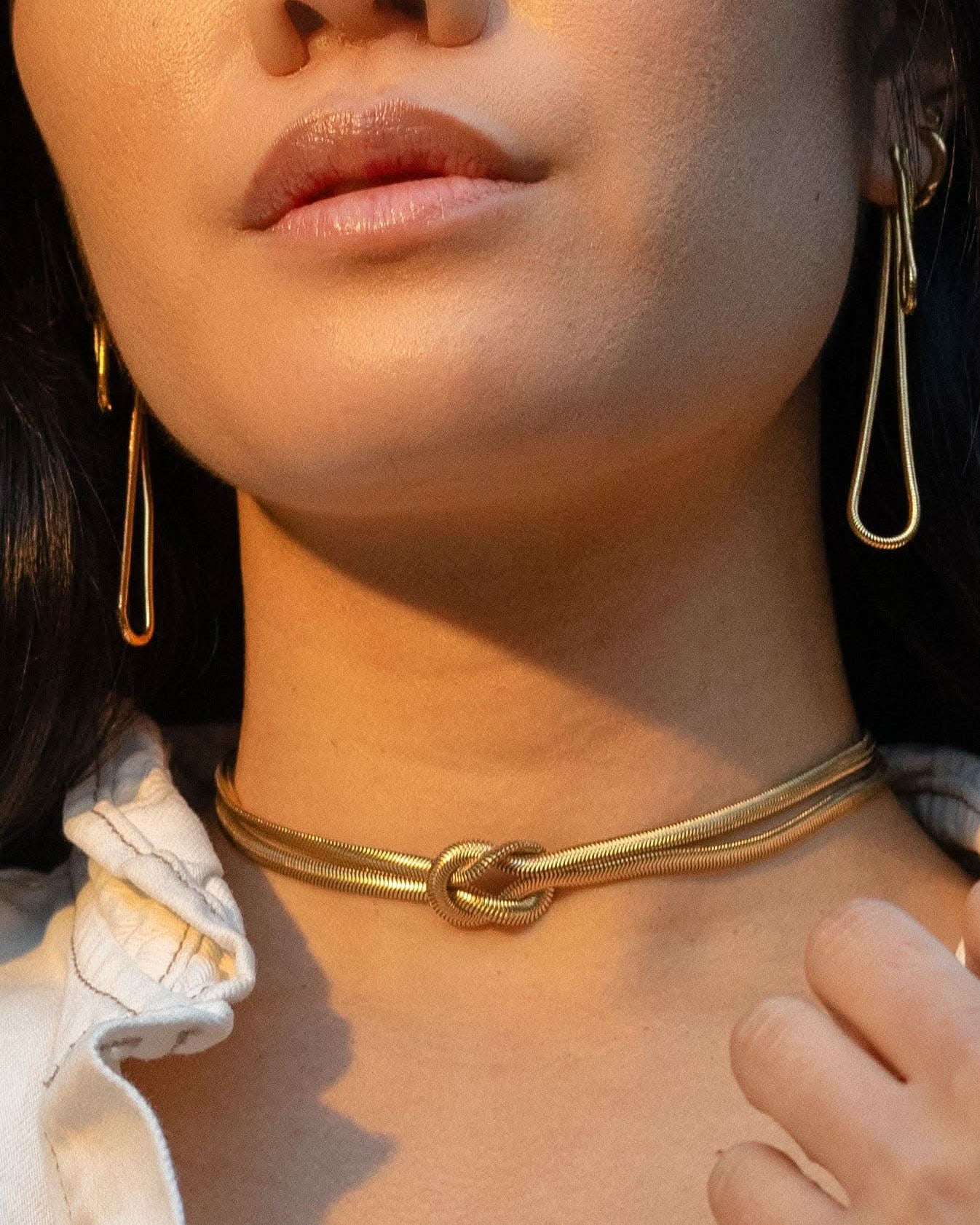 Woman wearing long abstract loop earrings and gold figure eight knot herringbone choker necklace