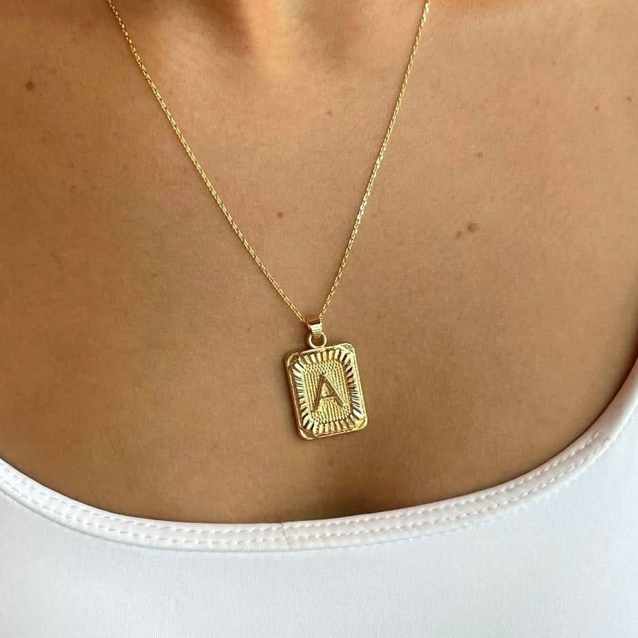 Woman wearing a letter A tarnish free gold initial charm necklace while wearing a white tank top.