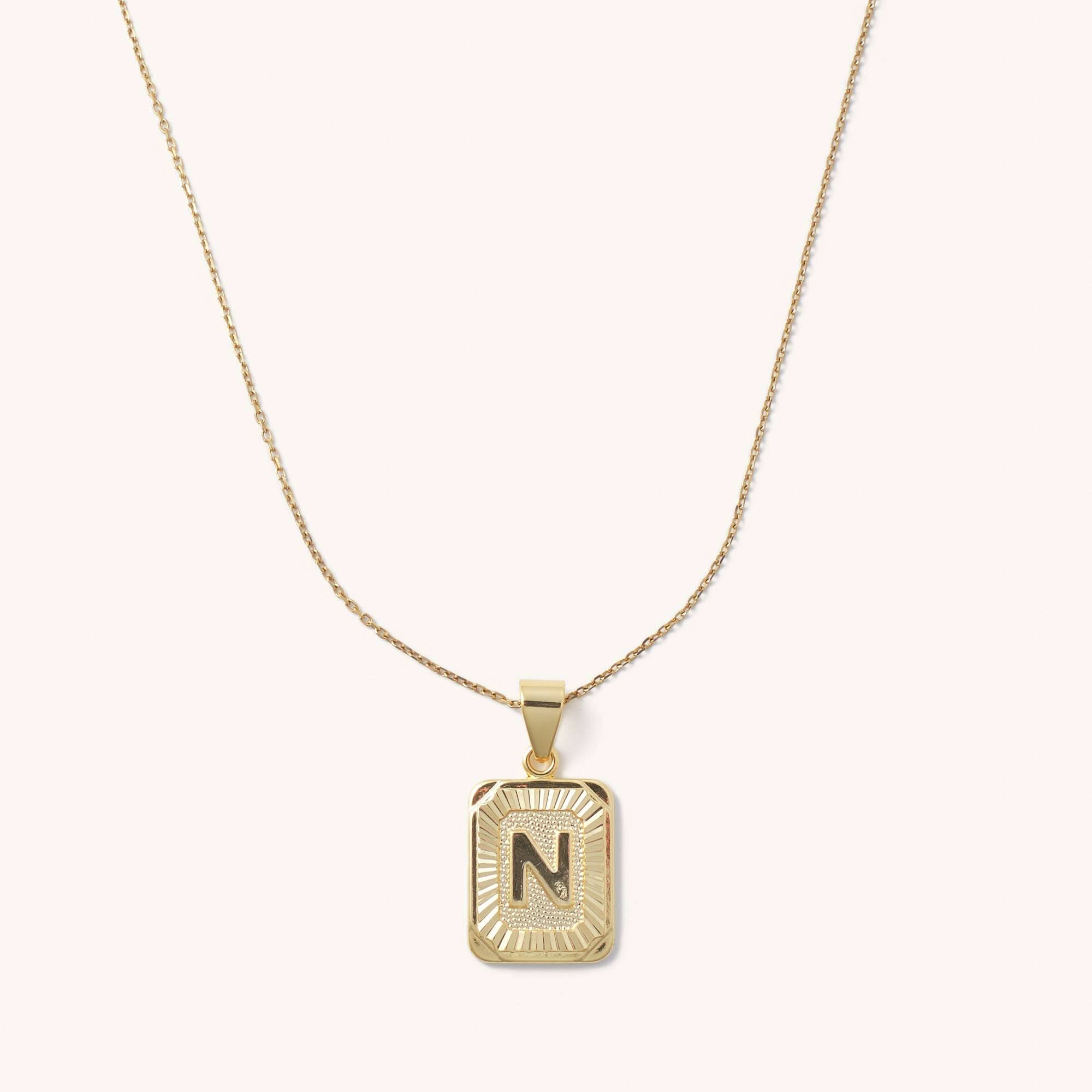 Letter N tarnish free gold initial charm necklace behind a blank background.
