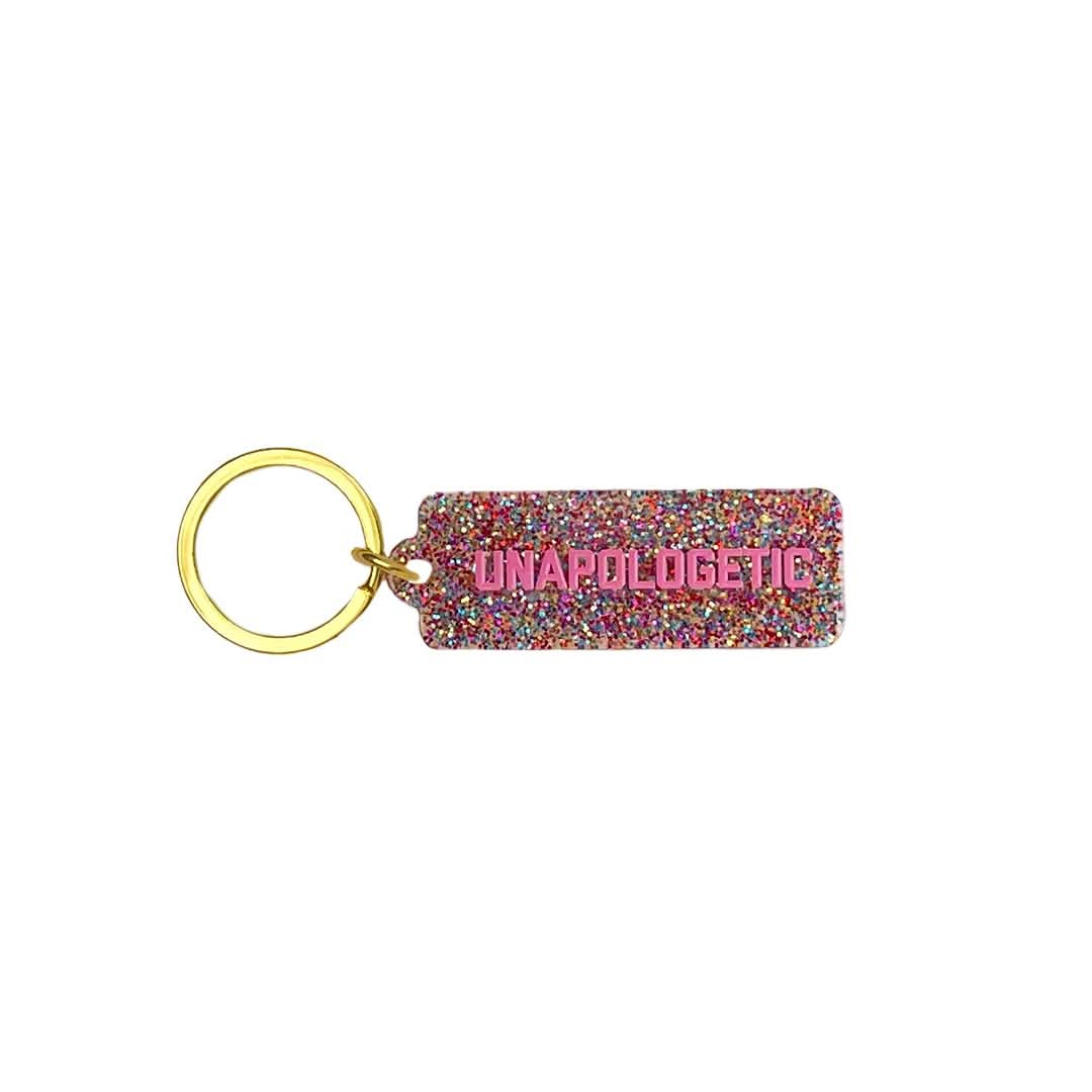 Keychain with 'UNAPOLOGETIC' text on a glittery tag with gold ring.