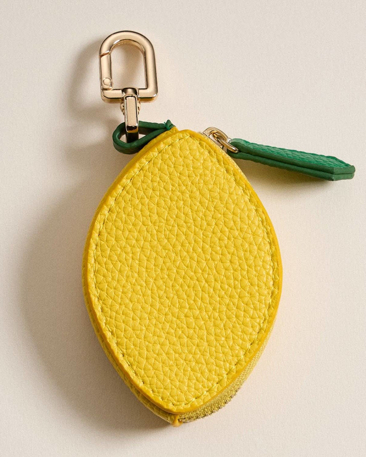 Yellow lemon-shaped keychain with a green strap on a beige background