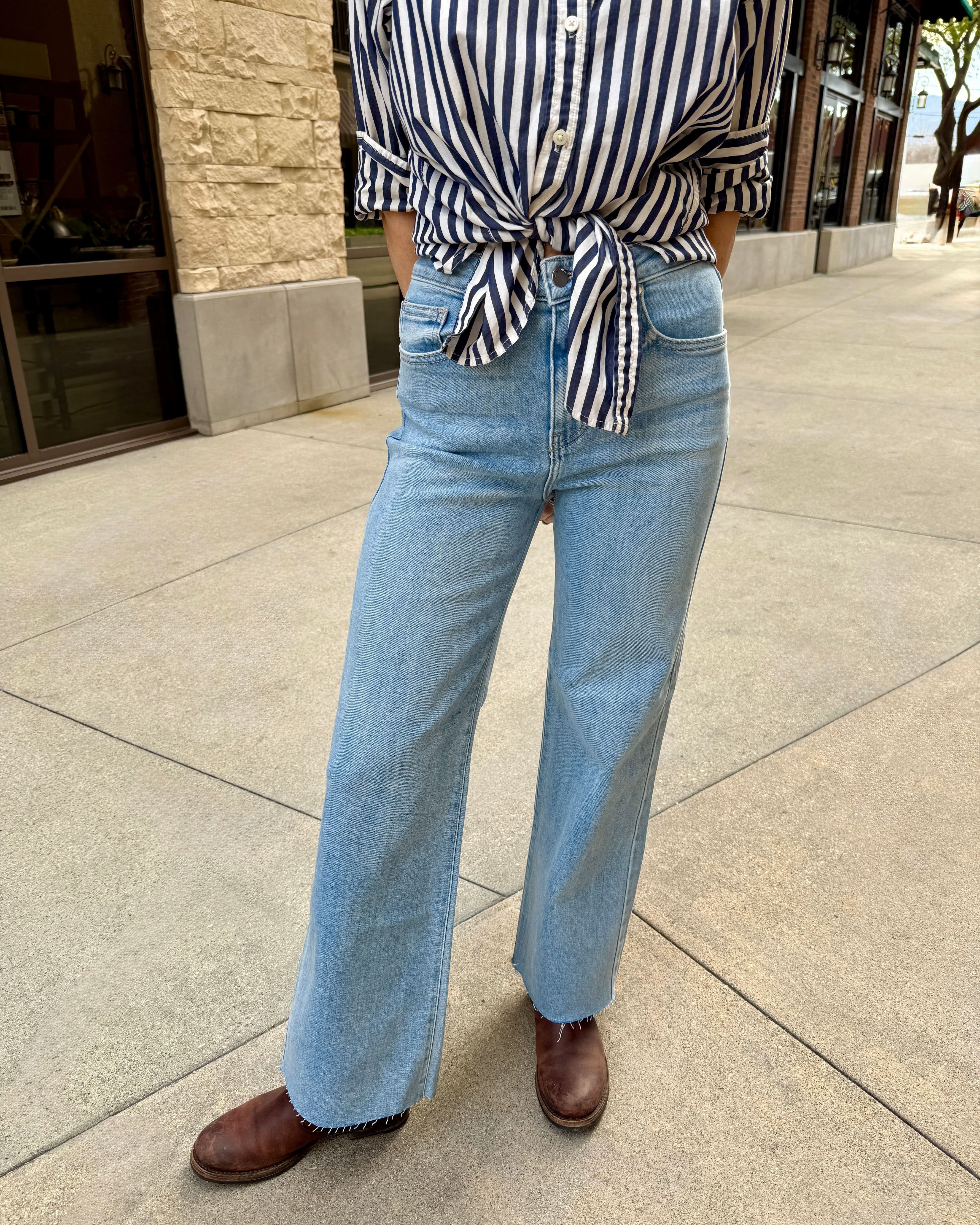 Woman standing outside wearing light wash raw hem jeans with navy blue