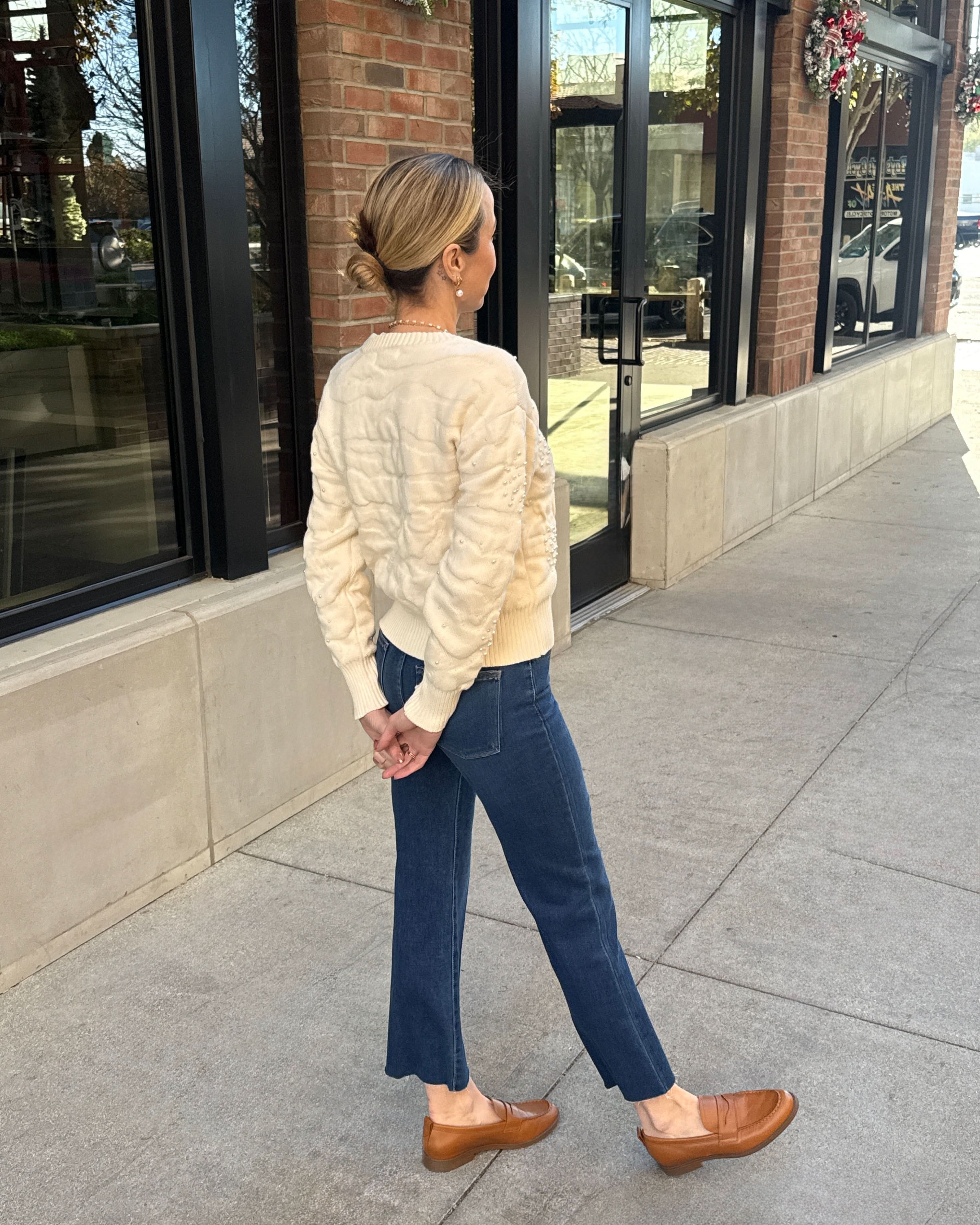 Woman wearing a cream sweater, blue jeans, and brown shoes.