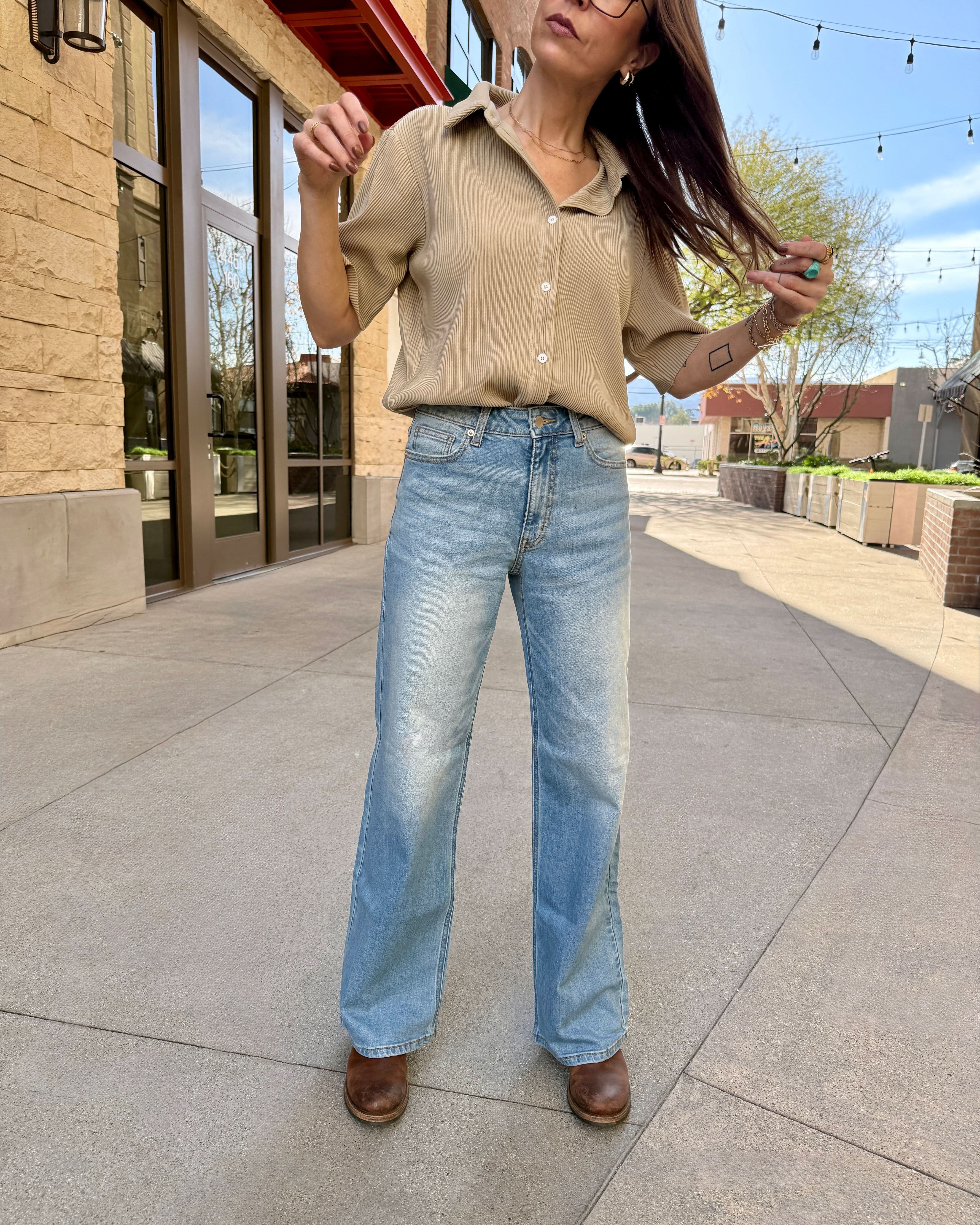 Woman in beige shirt and blue jeans standing on a sidewalk