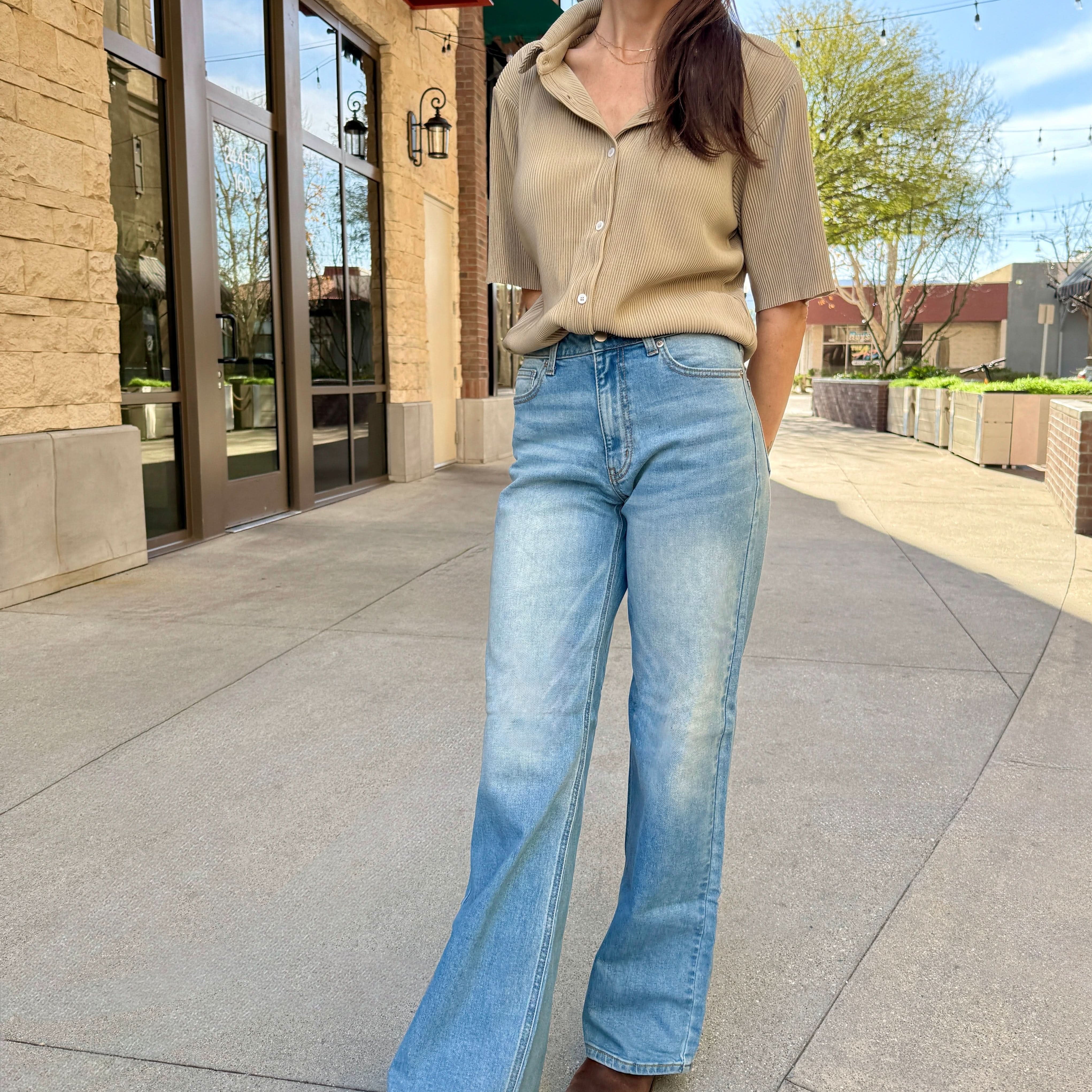 Woman wearing a beige top and blue jeans standing on a sidewalk.