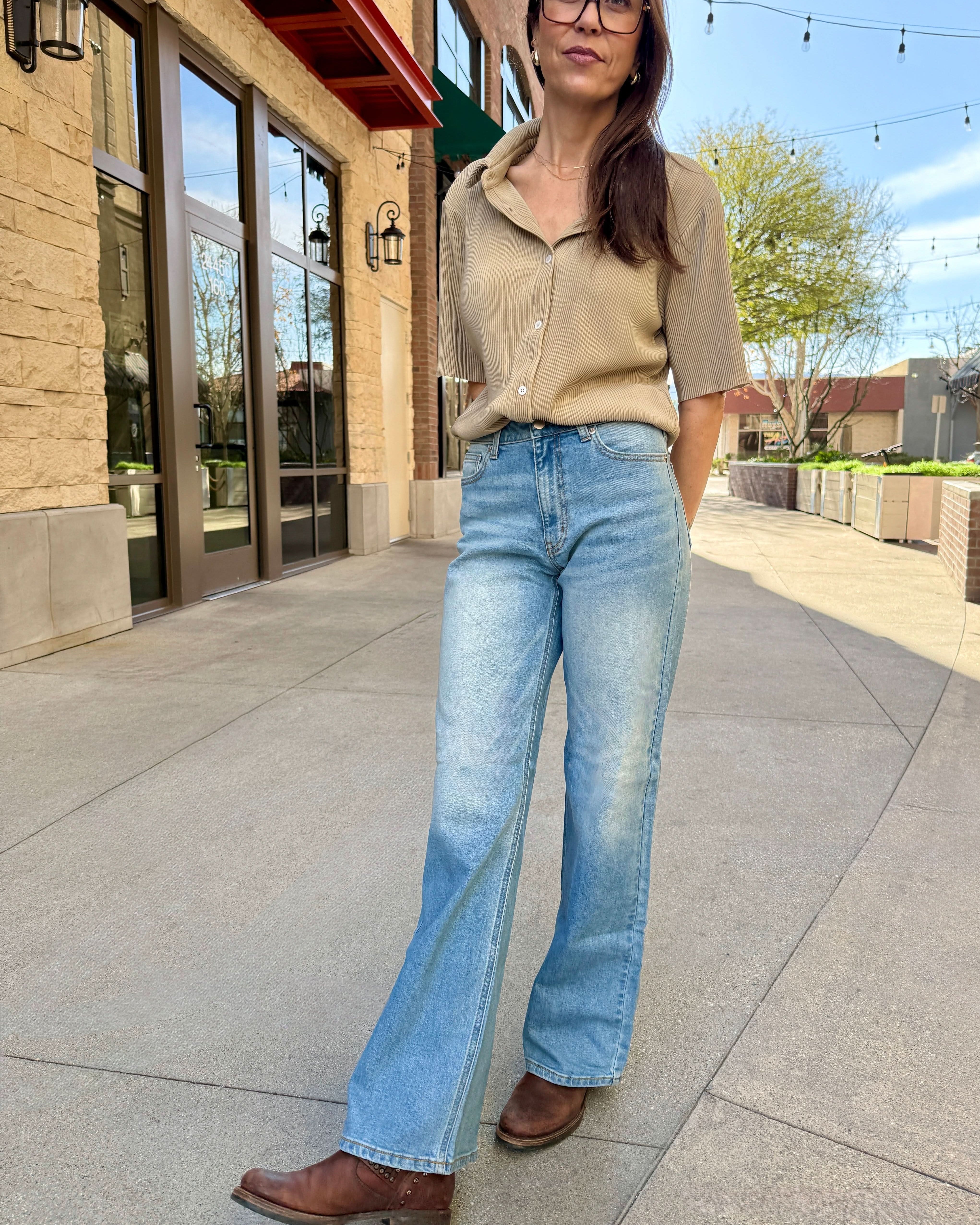 Woman wearing a beige top and blue jeans standing on a sidewalk.