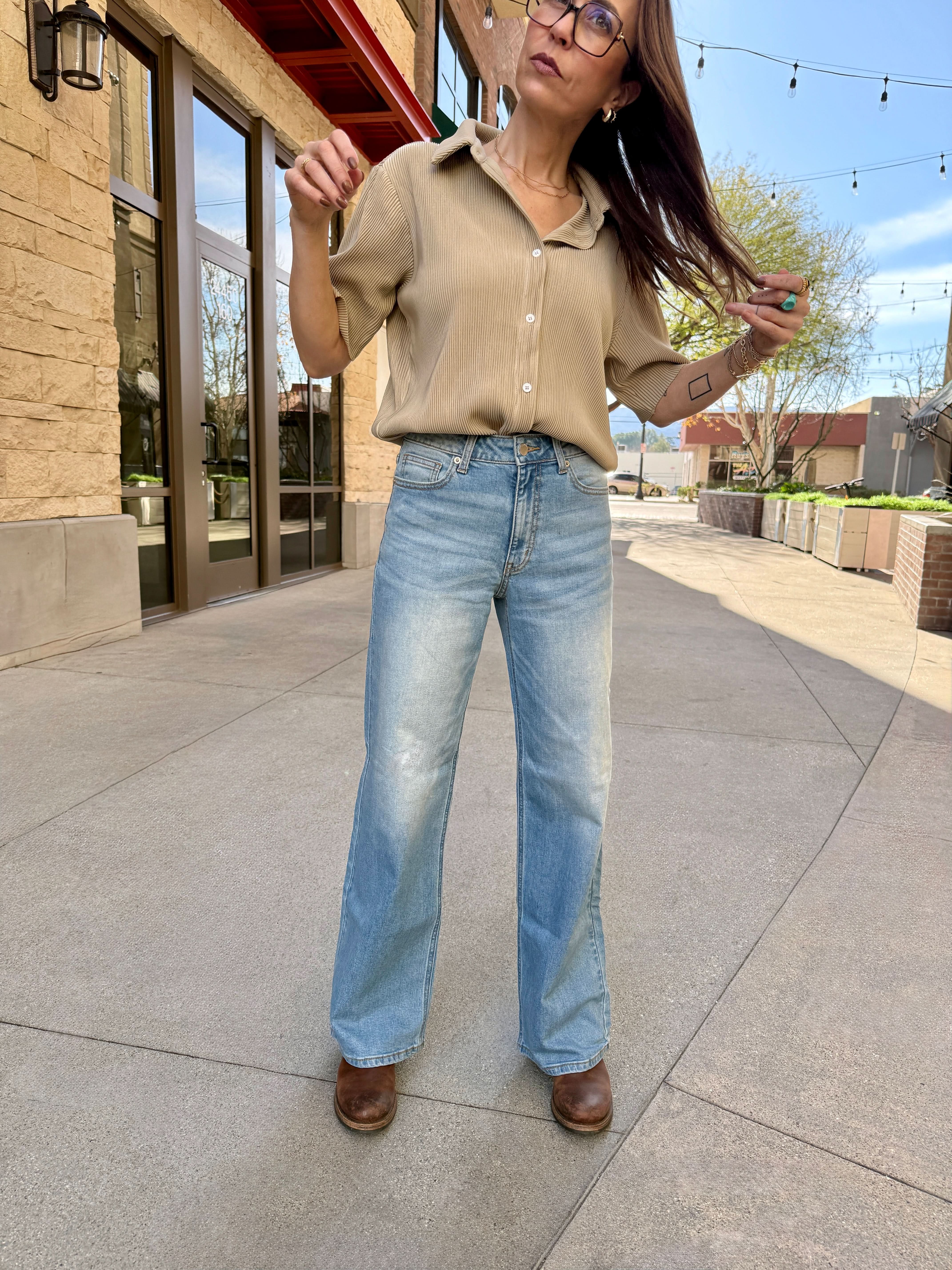 Woman in beige shirt and blue jeans standing on a sidewalk
