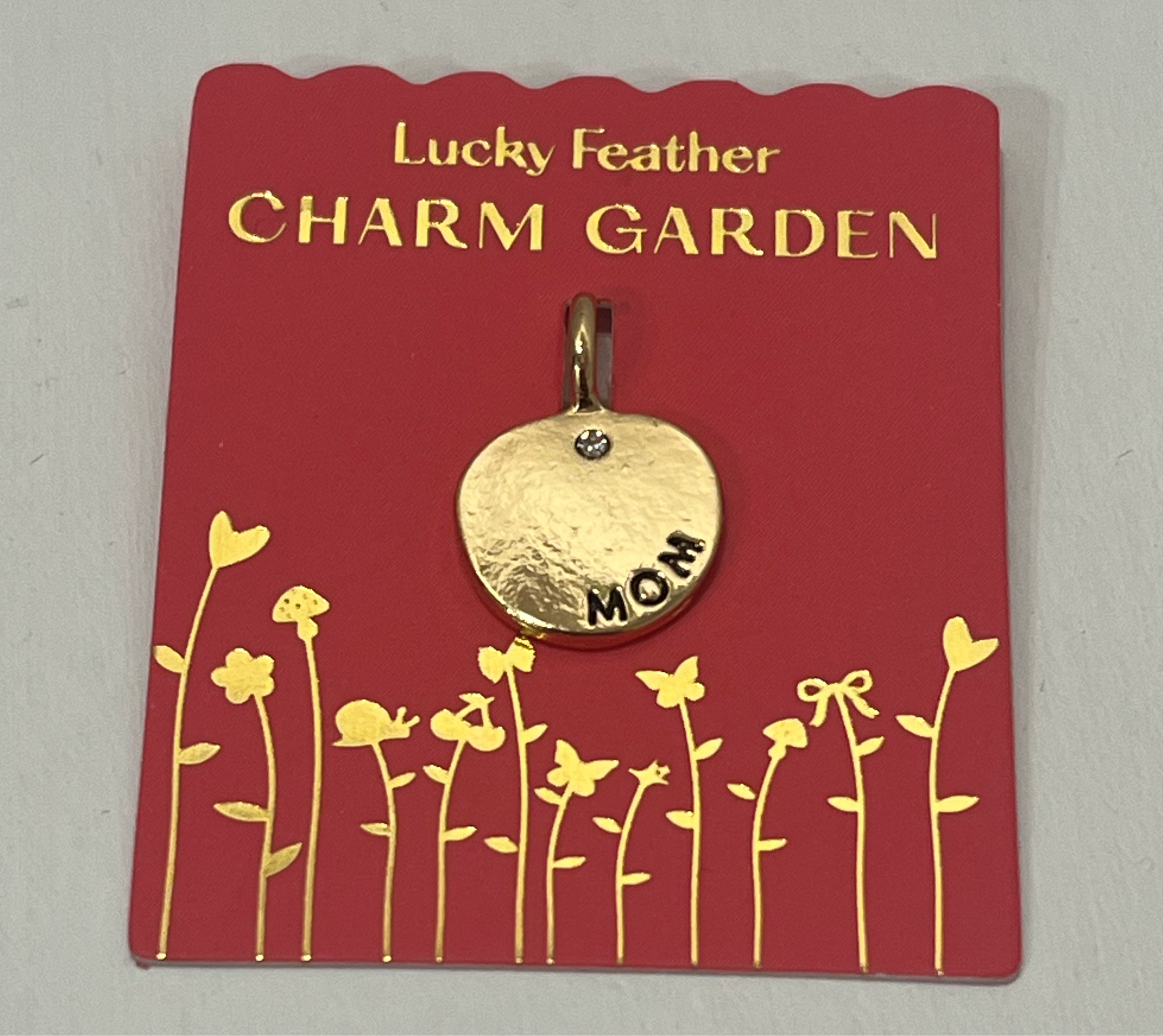 Gold 'Mom' charm on a red card with 'Lucky Feather Charm Garden' text