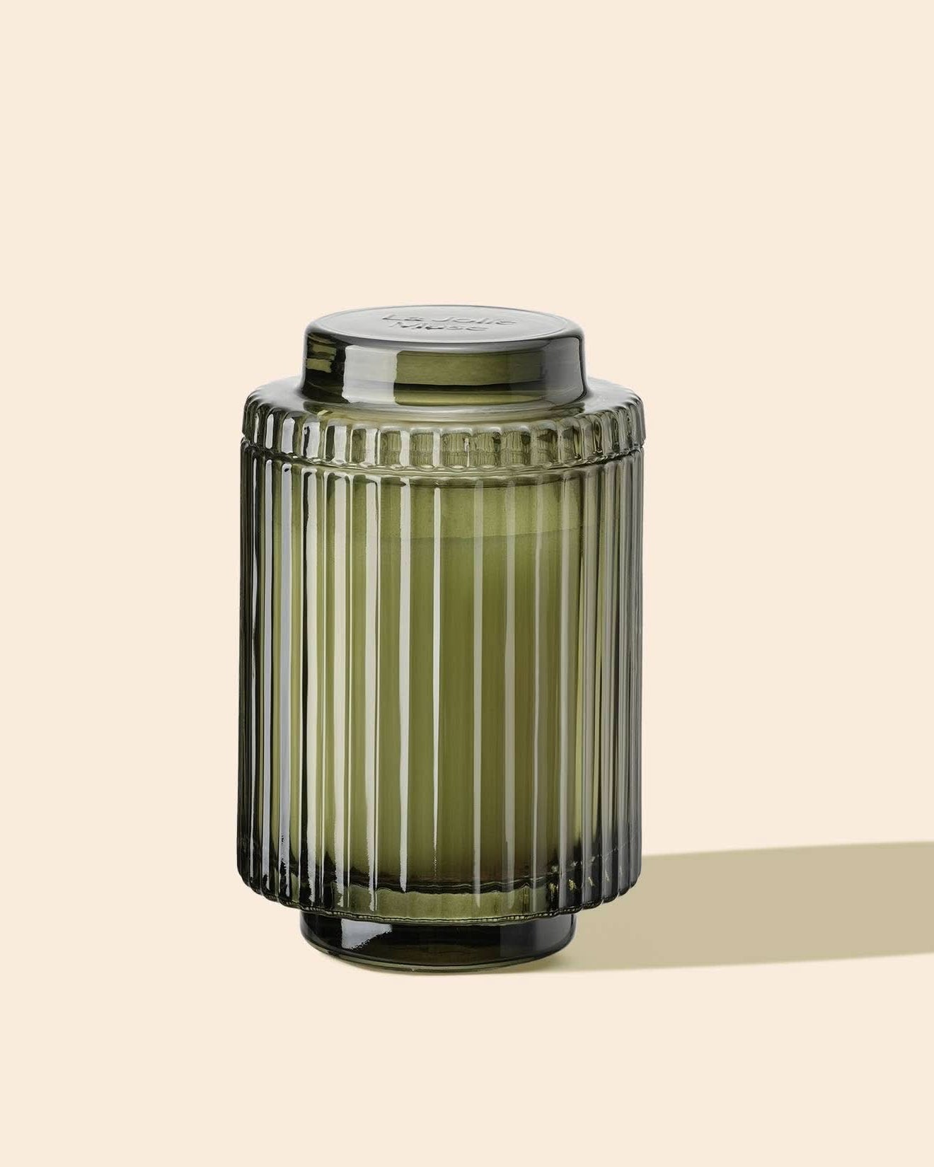 Green ribbed glass jar with a lid on a beige background