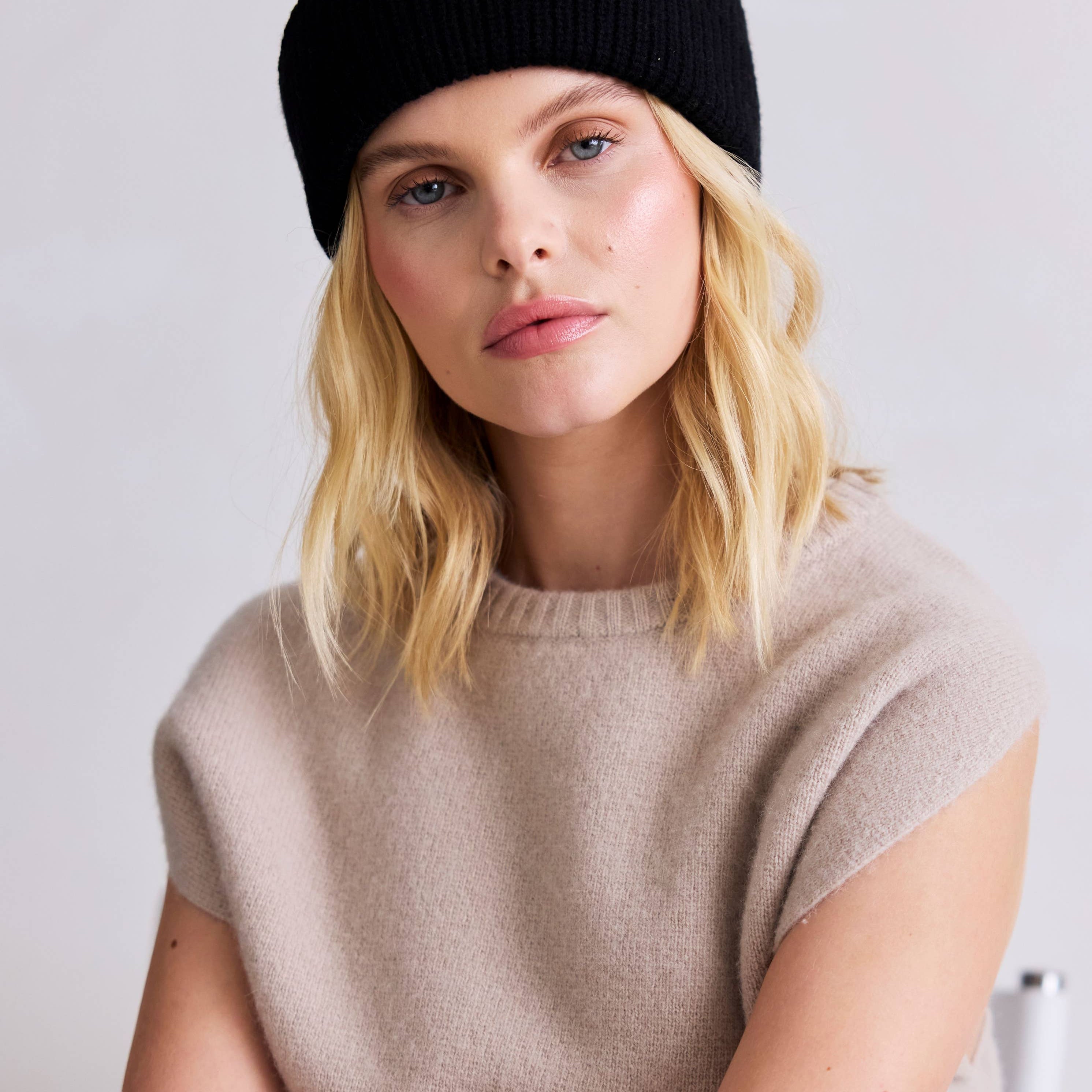 Woman wearing a black beanie and beige sweater against a white background