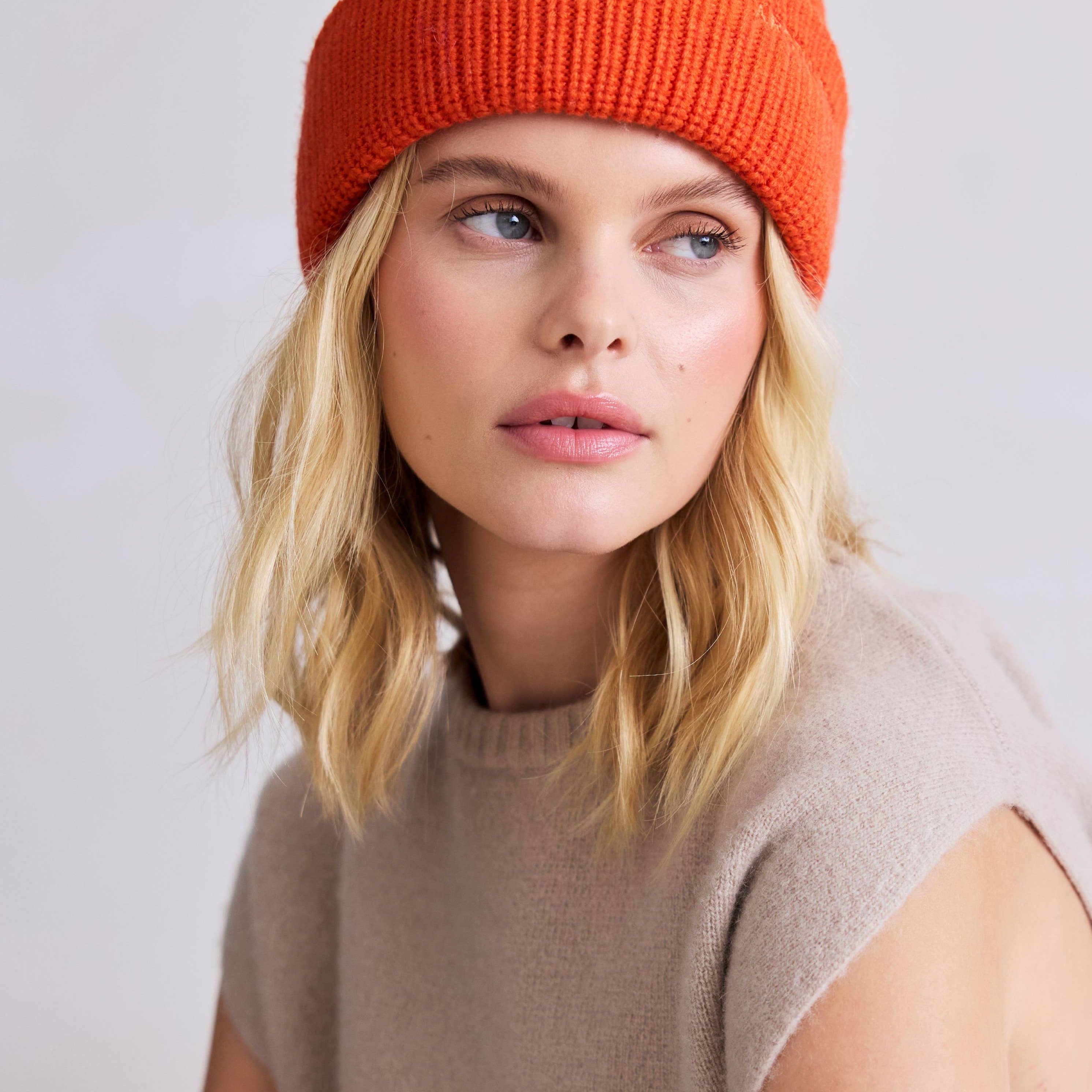 Woman wearing an orange knit beanie against a plain background