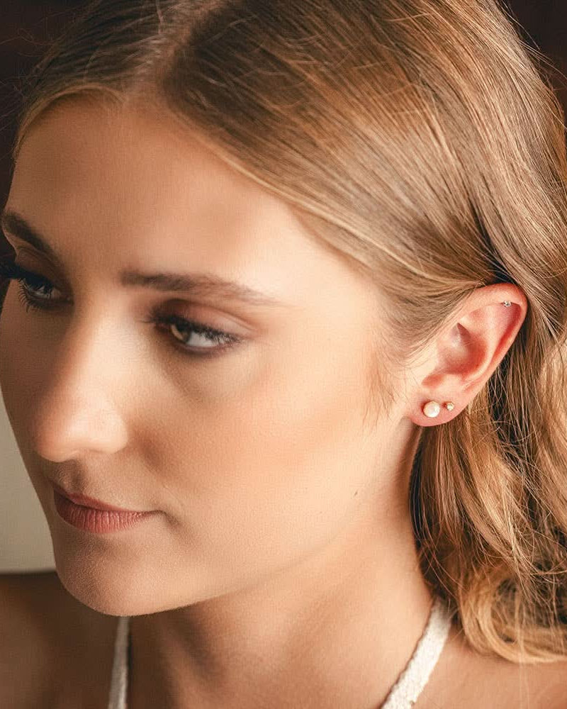 Close-up of a woman with blonde hair and earrings, wearing a white top.