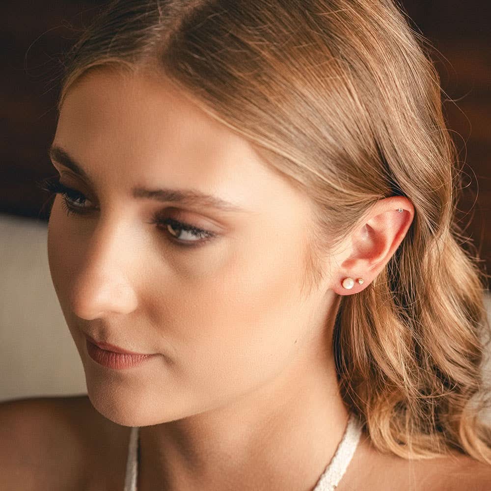 Close-up of a woman with blonde hair and earrings, wearing a white top.