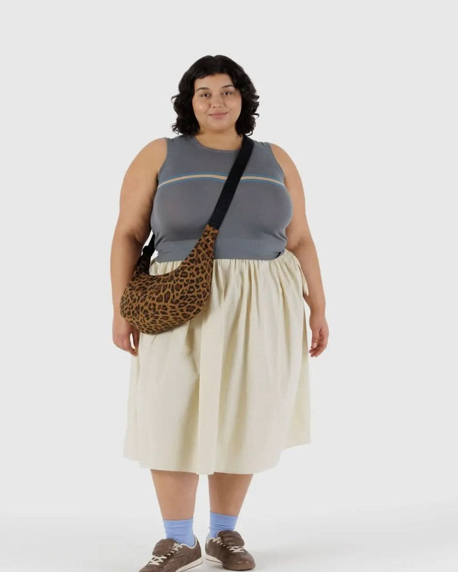 Woman carrying BAGGU leopard print purse with black strap while wearing gray tank top and white skirt