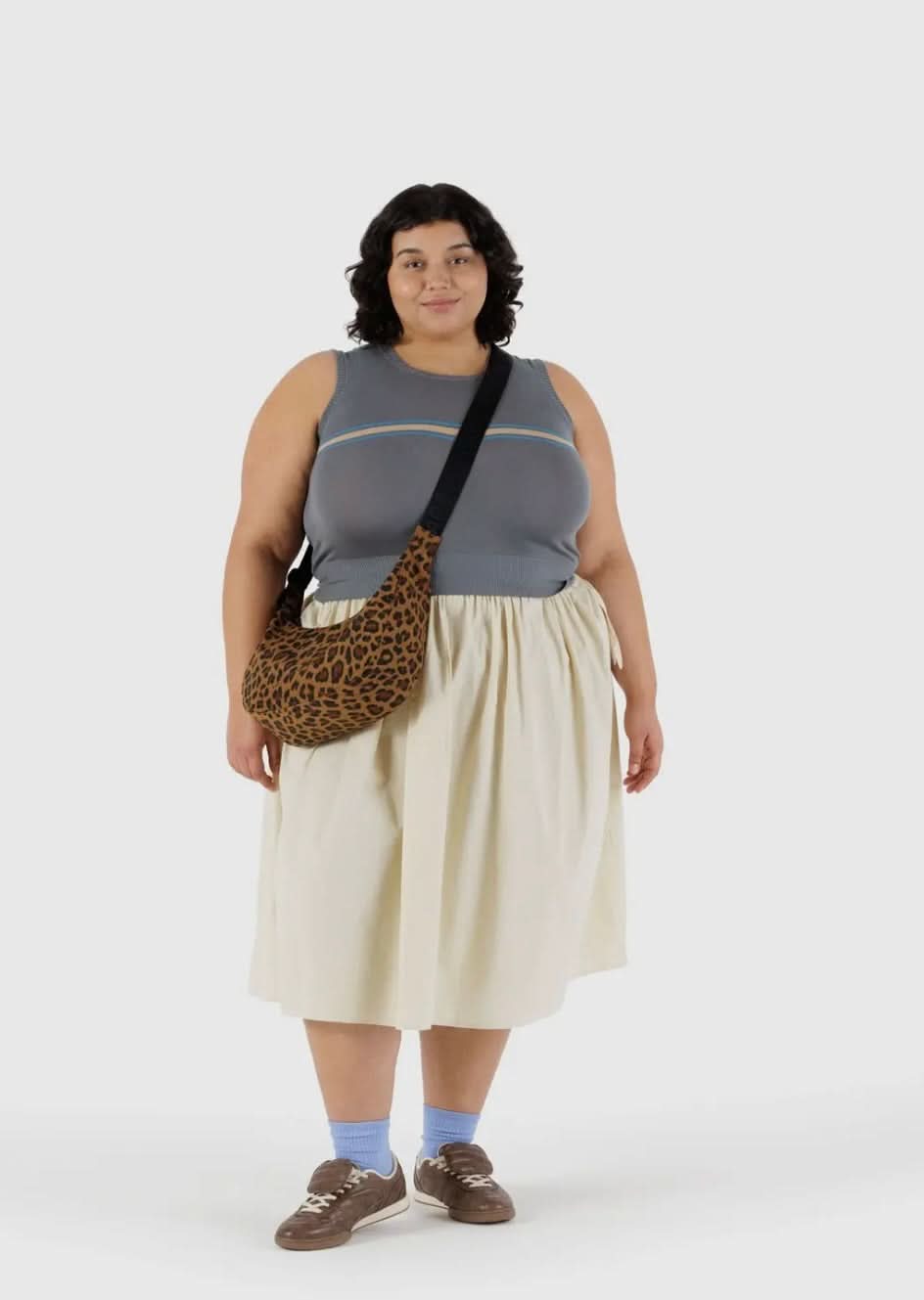 Woman carrying BAGGU leopard print purse with black strap while wearing gray tank top and white skirt