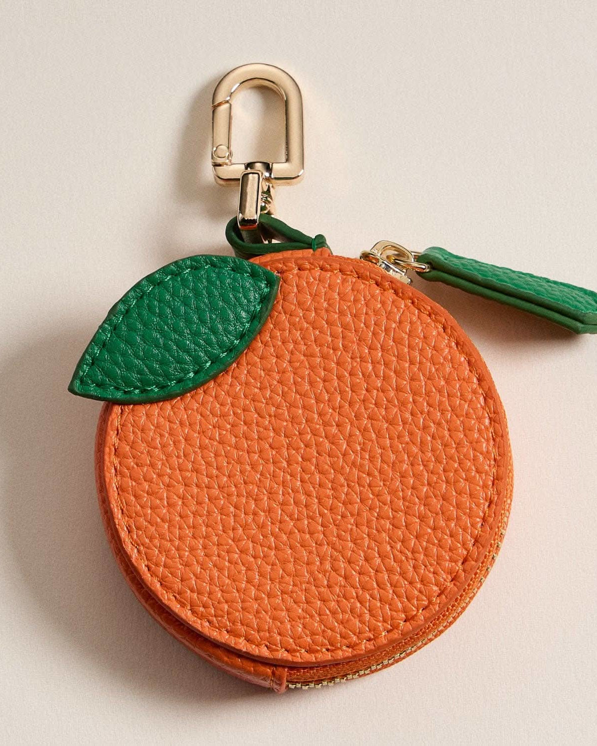 Orange-shaped keychain with green leaf on a beige background