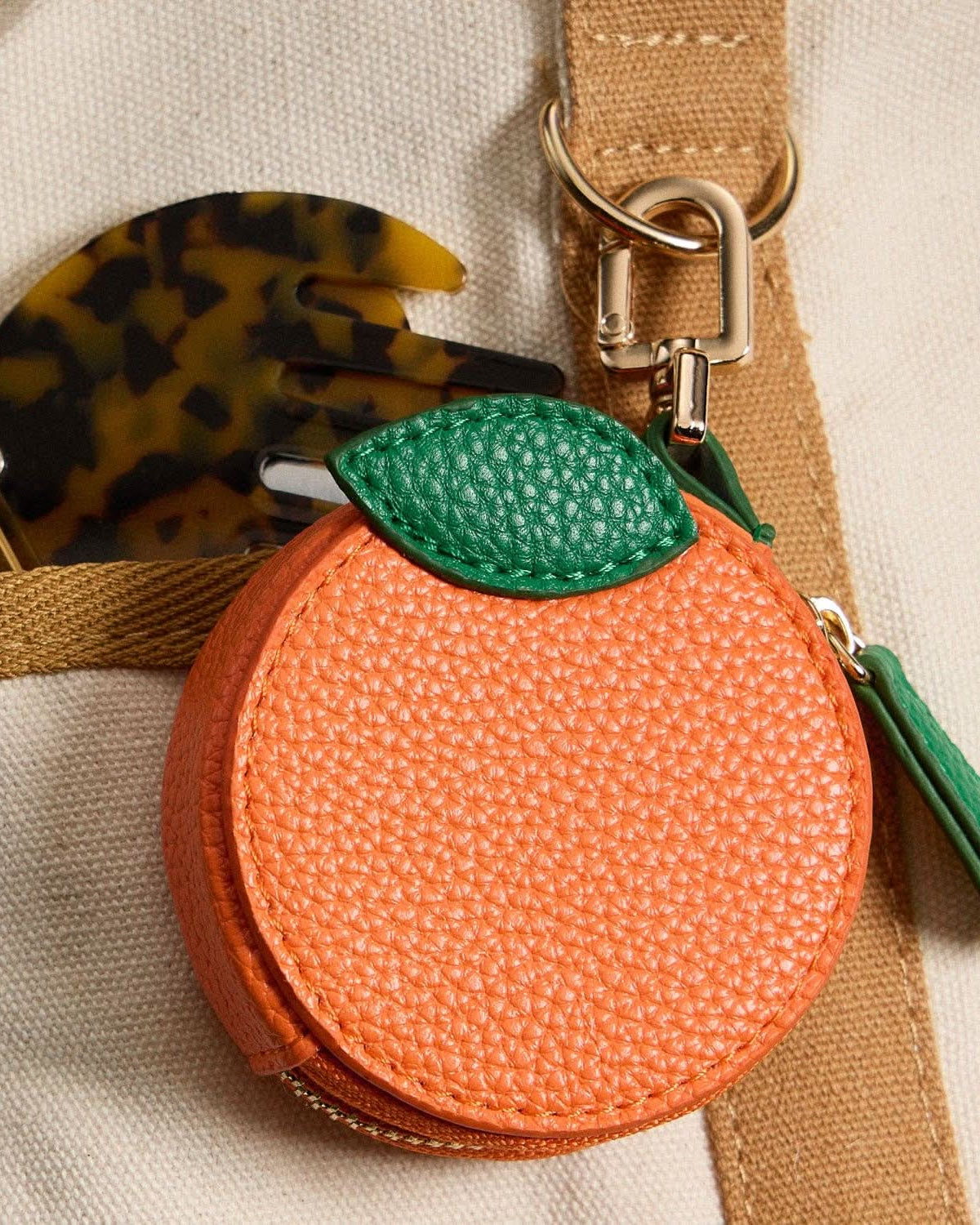 Orange fruit-shaped keychain with a green leaf on a beige background