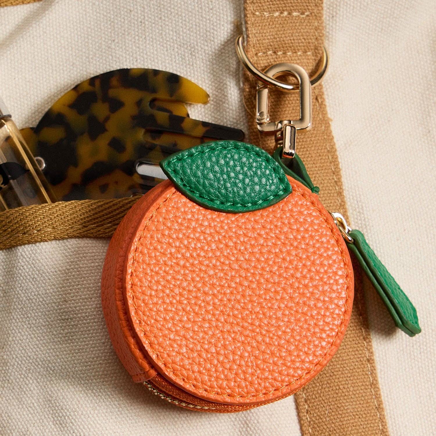 Orange fruit-shaped keychain with a green leaf on a beige background