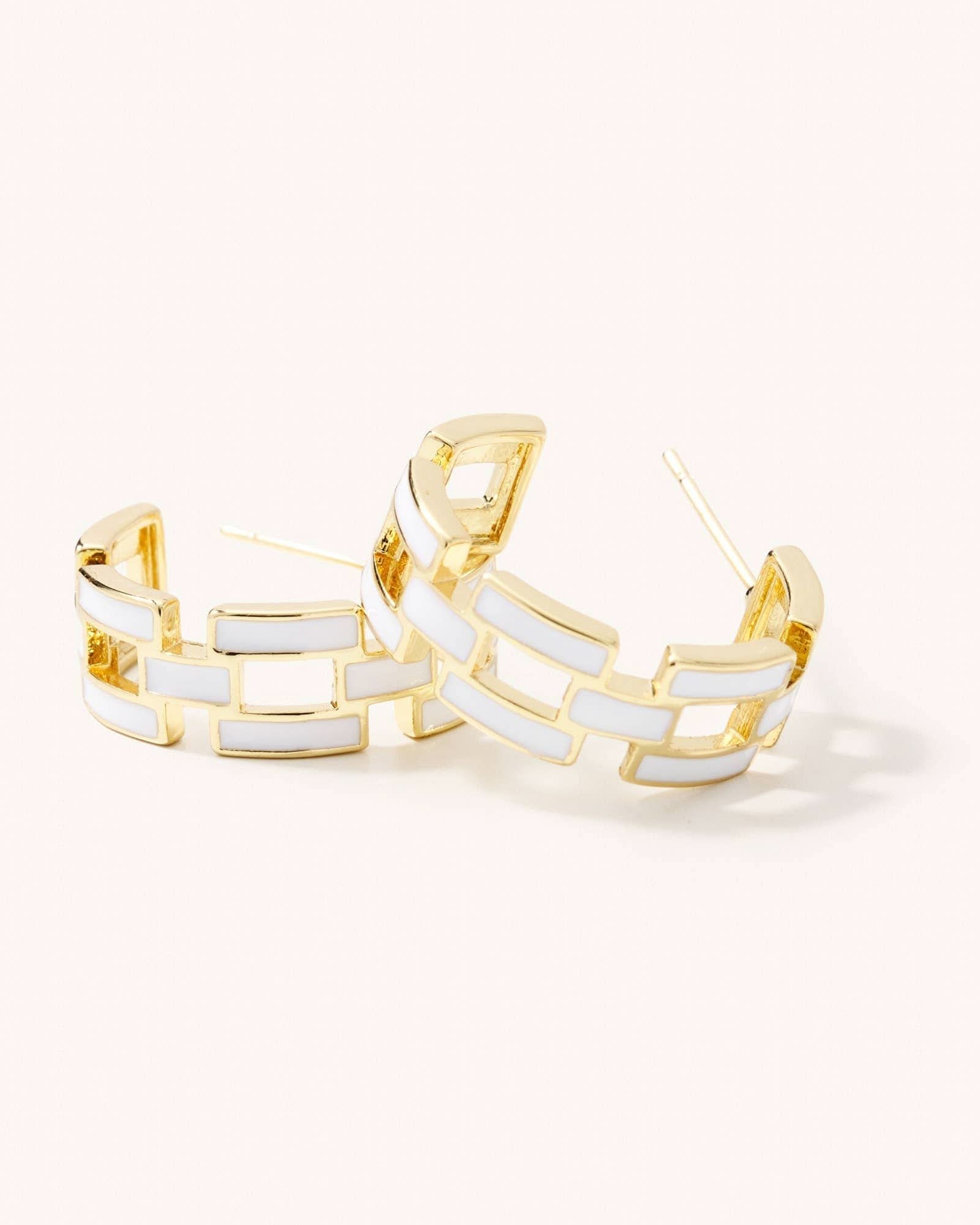 Gold hoop earrings with white geometric design on a light beige background