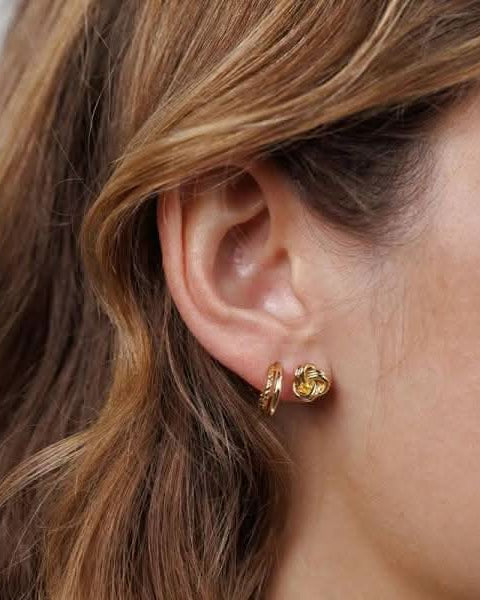 model wearing two earrings one gold double hoop and one twisted knot stud