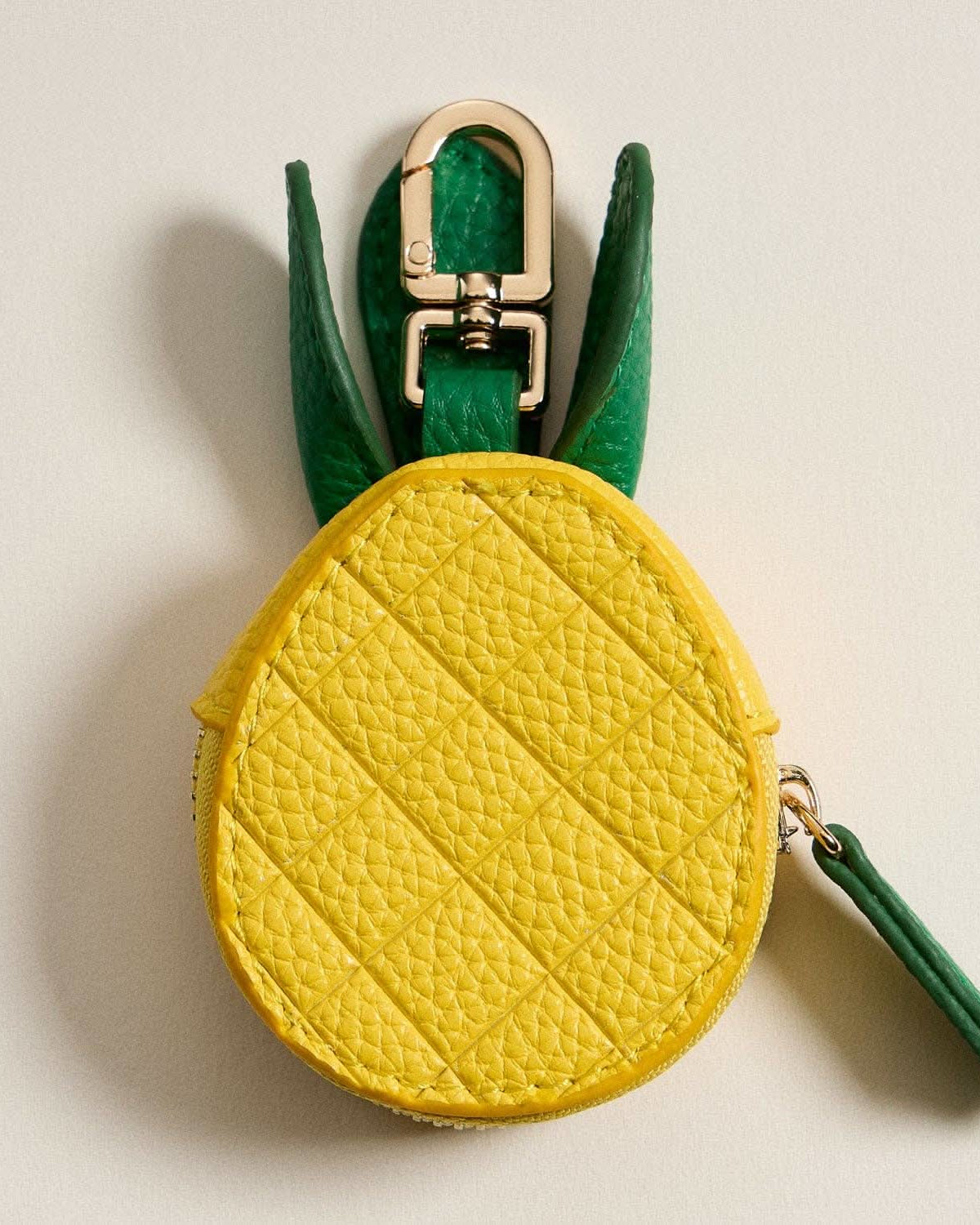 Pineapple-shaped keychain with yellow body and green leaves on a beige background