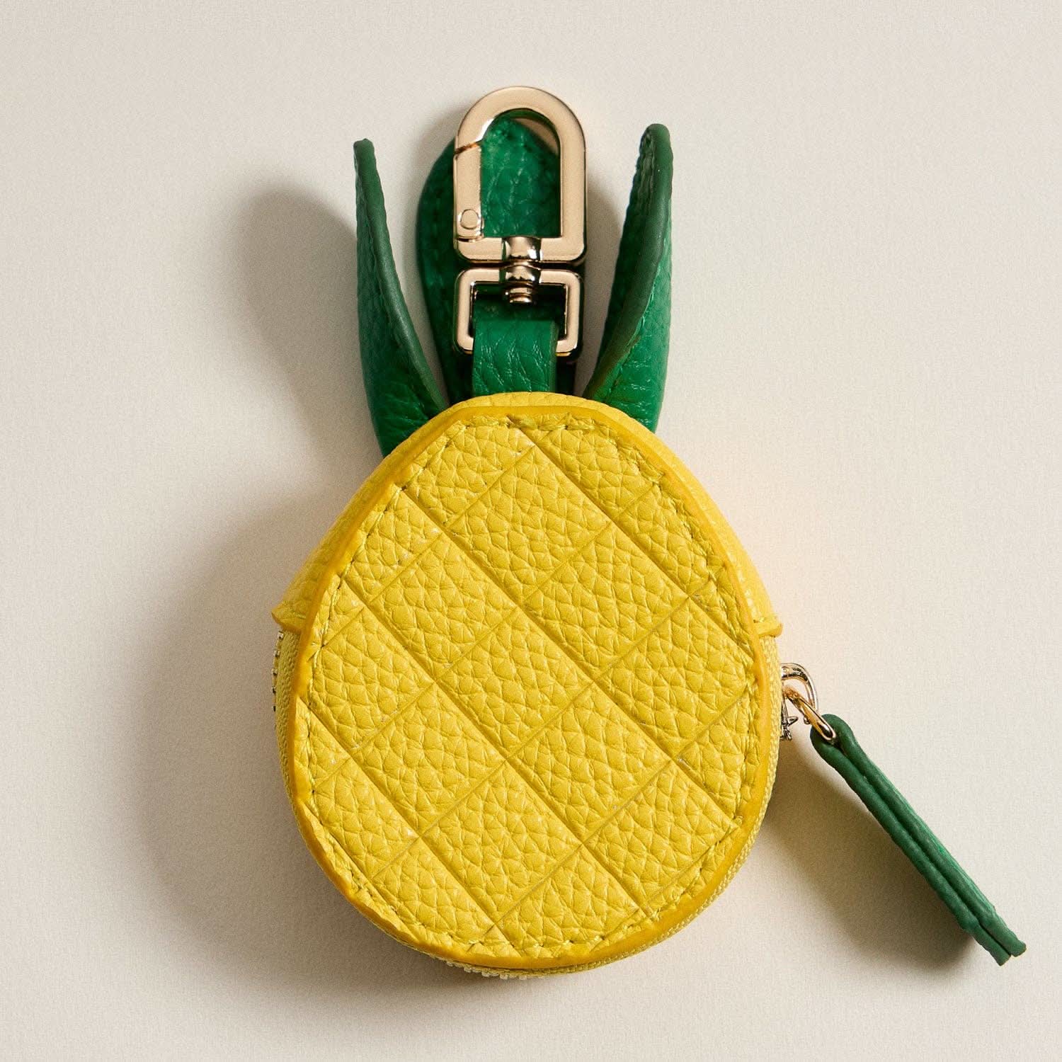 Pineapple-shaped keychain with yellow body and green leaves on a beige background