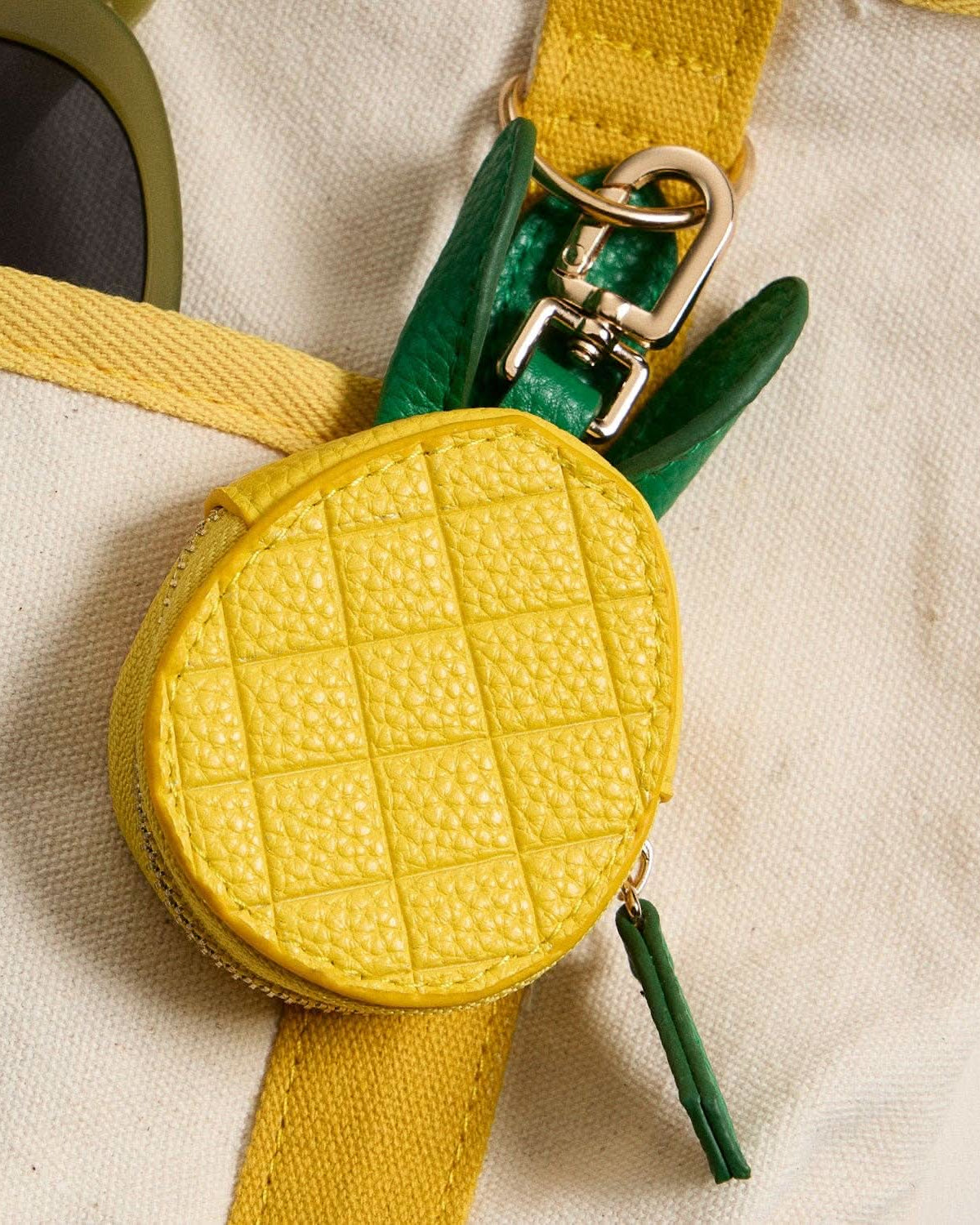 Yellow textured pouch with green strap on a beige background