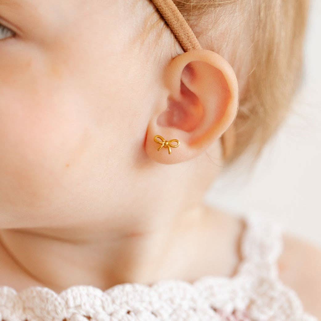 Gold bow-shaped earring worn by a person with a blurred background