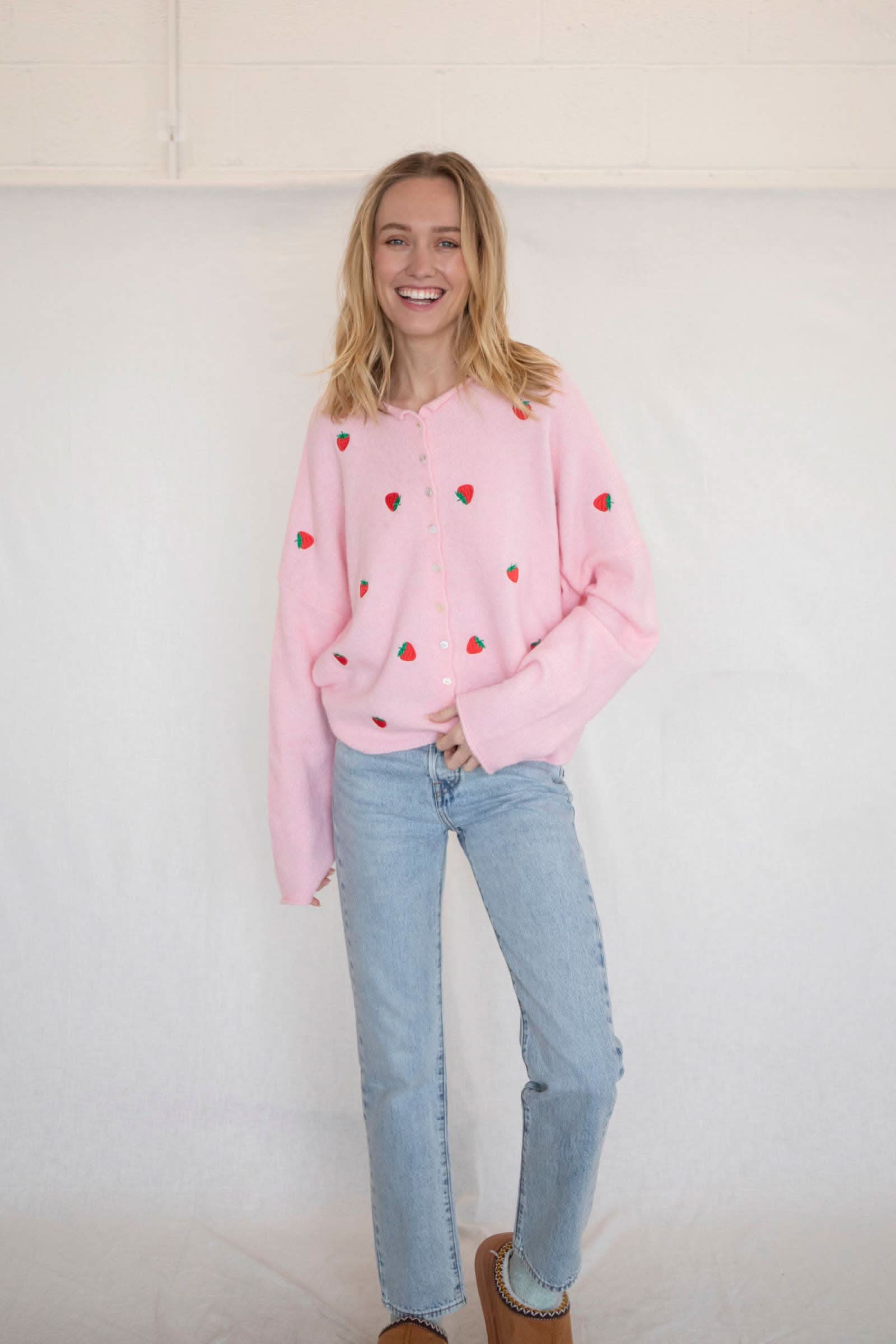 Woman wearing a pink button down cardigan with strawberries and blue jeans