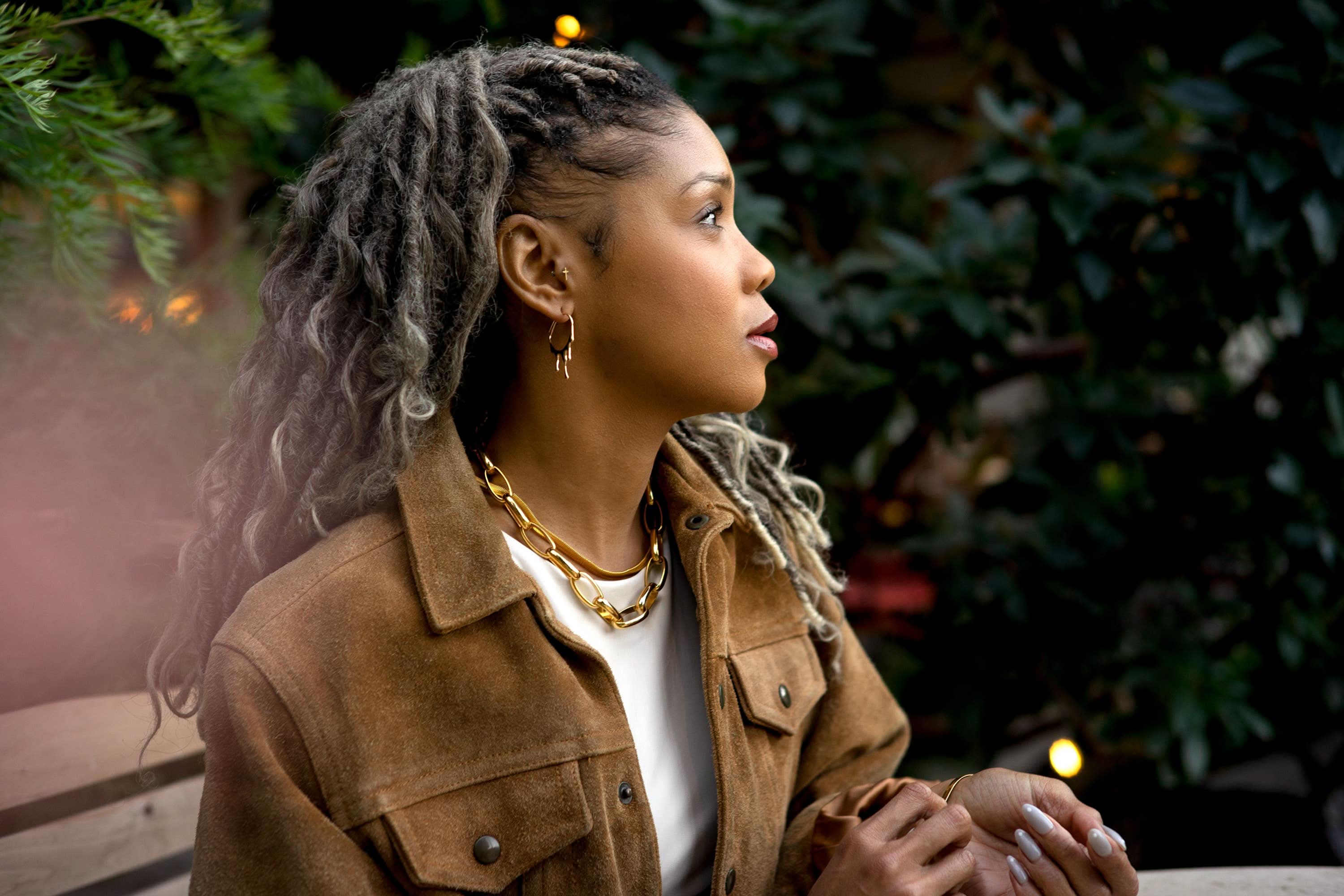 Woman with braided hair wearing a brown jacket outdoors