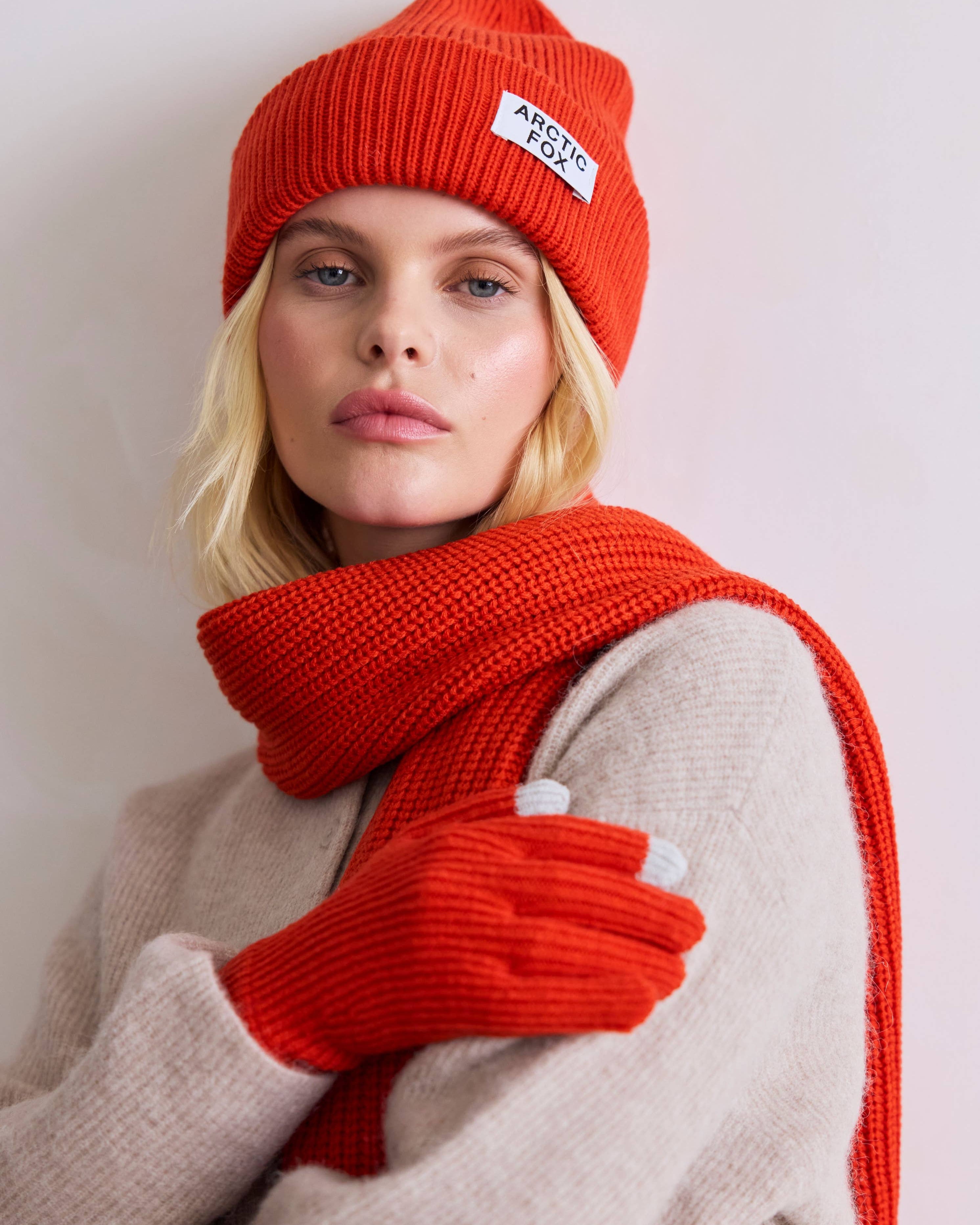 Person wearing a red knit hat, scarf, and gloves with a visible brand logo on a light background