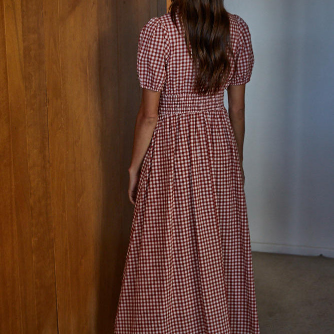 Woman in a red and white checkered dress standing in a room with wooden walls.