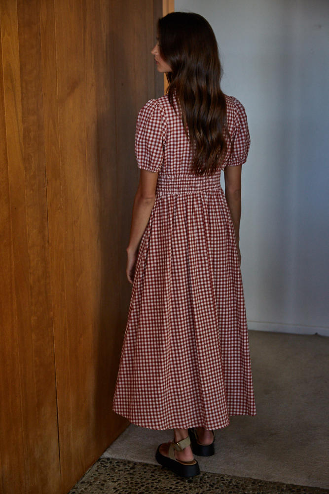 Woman in a red and white checkered dress standing in a room with wooden walls.