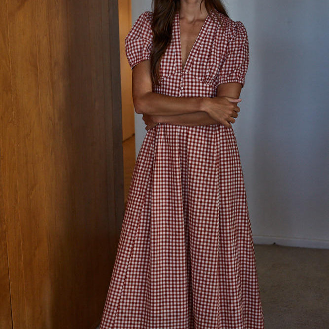 Woman wearing a red and white checkered dress standing against a wooden wall.