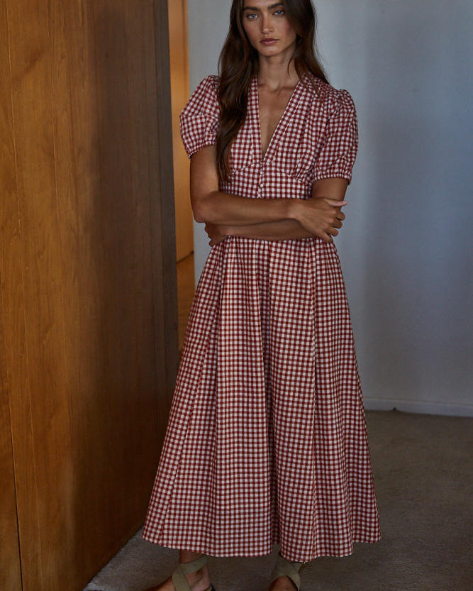 Woman wearing a red and white checkered dress standing against a wooden wall.