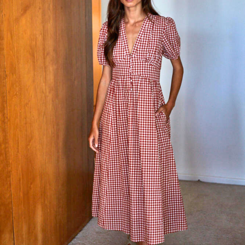 Woman wearing a red and white checkered dress standing against a wooden wall.