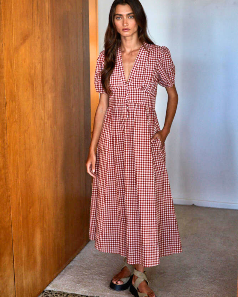 Woman wearing a red and white checkered dress standing against a wooden wall.
