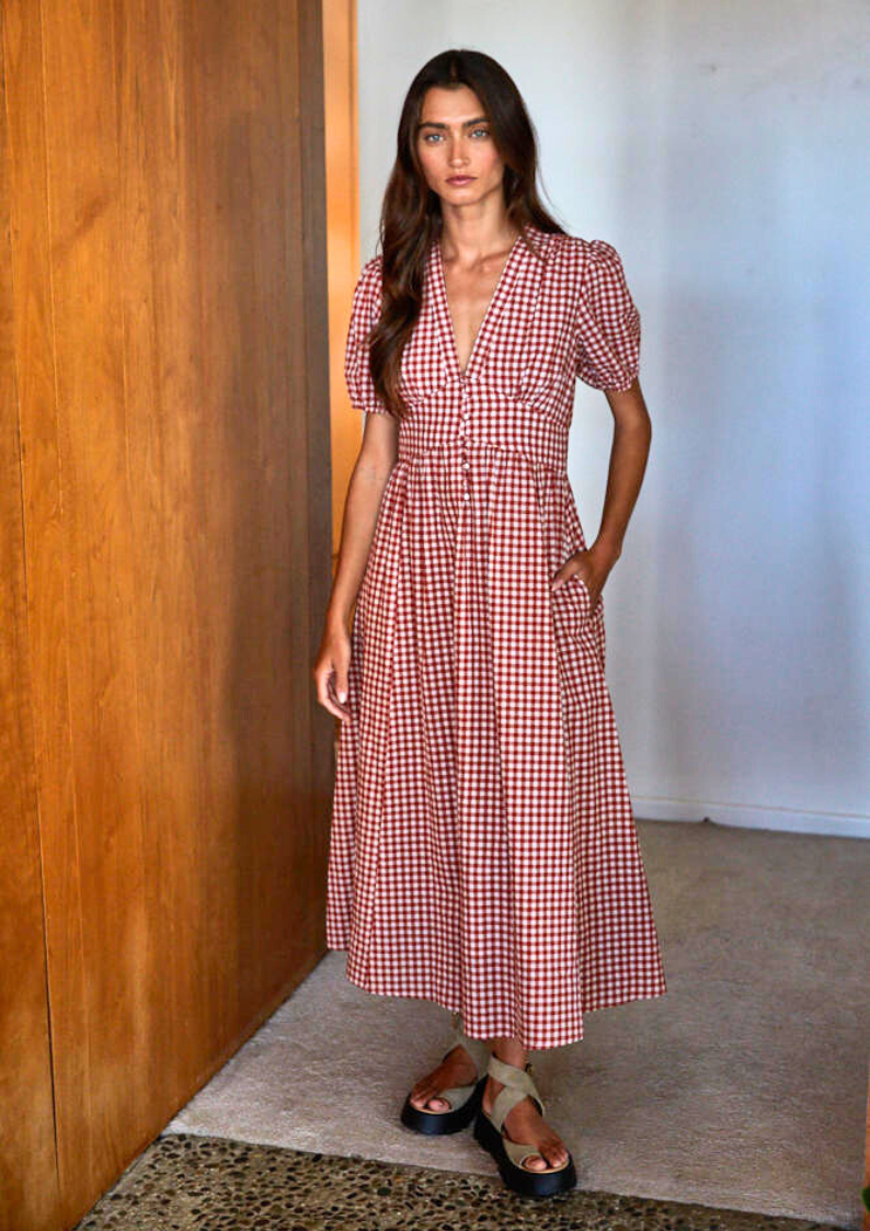 Woman wearing a red and white checkered dress standing against a wooden wall.