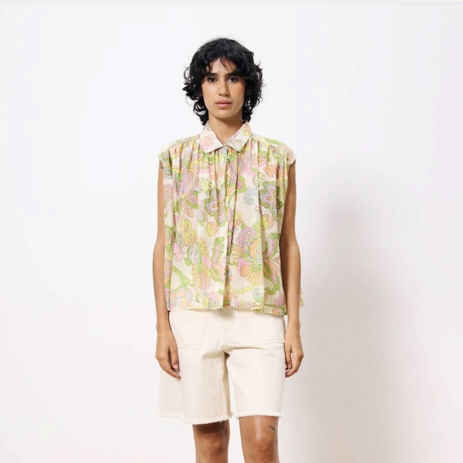 Woman wearing flowing sleeveless pastel floral blouse with collar paired with white Bermuda shorts