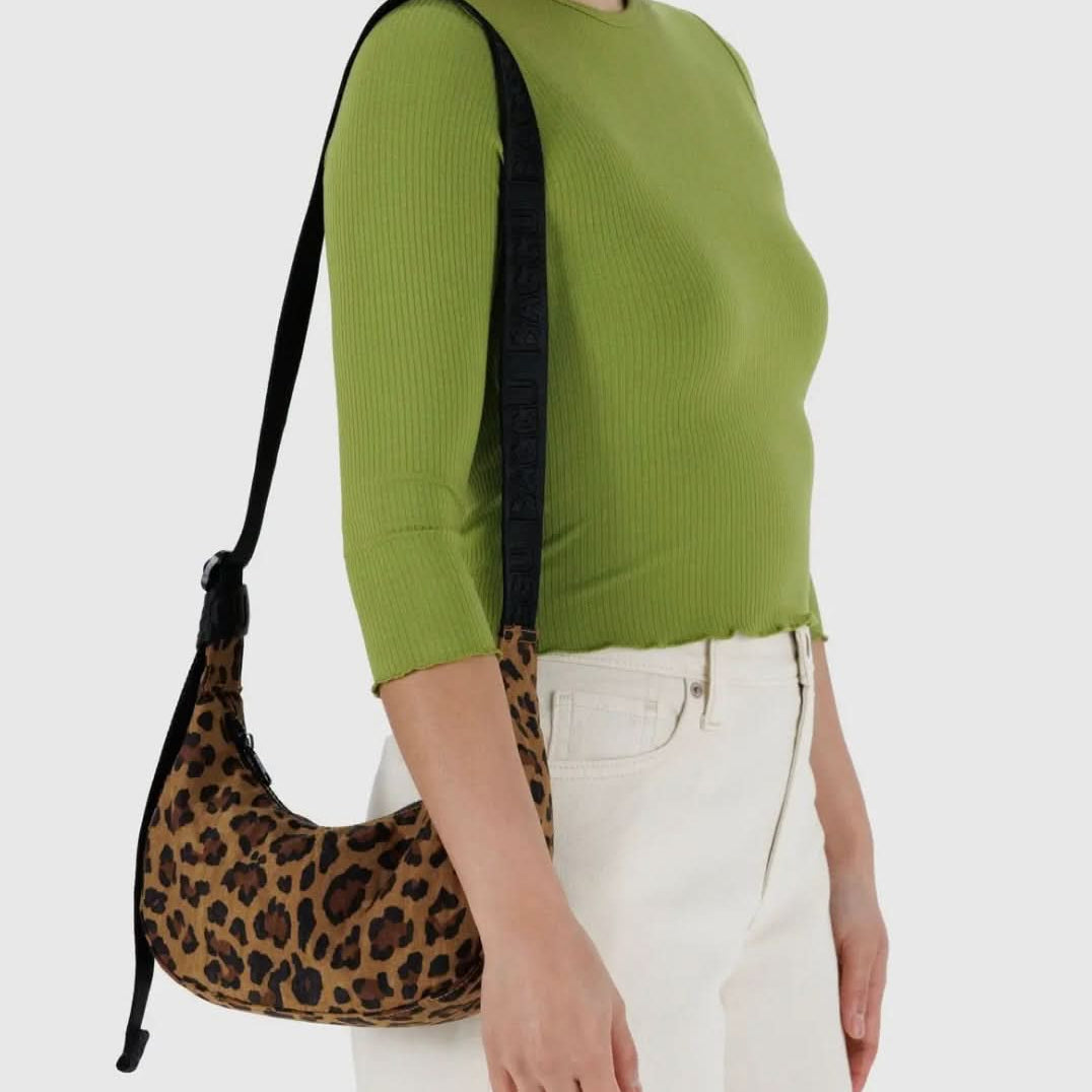 Woman carrying BAGGU leopard nylon bag with black strap while wearing green shirt and white jeans