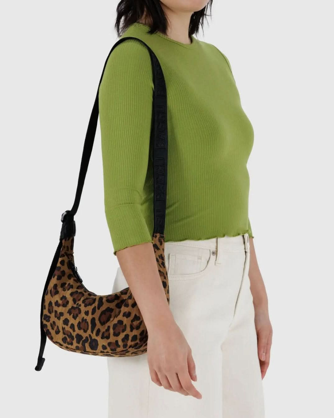 Woman carrying BAGGU leopard nylon bag with black strap while wearing green shirt and white jeans