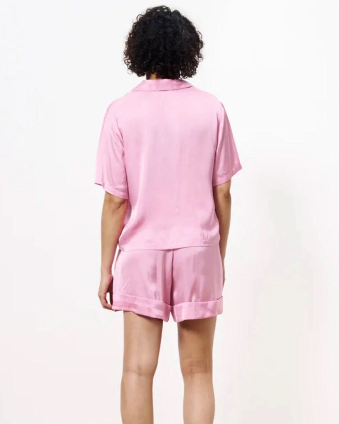 Woman turned away from the camera wearing a pink silky blouse button up with matching shorts