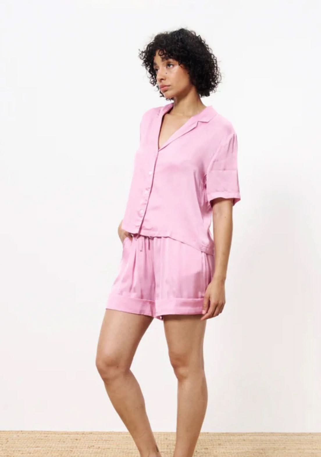 Woman wearing a pink silky blouse button up with matching shorts